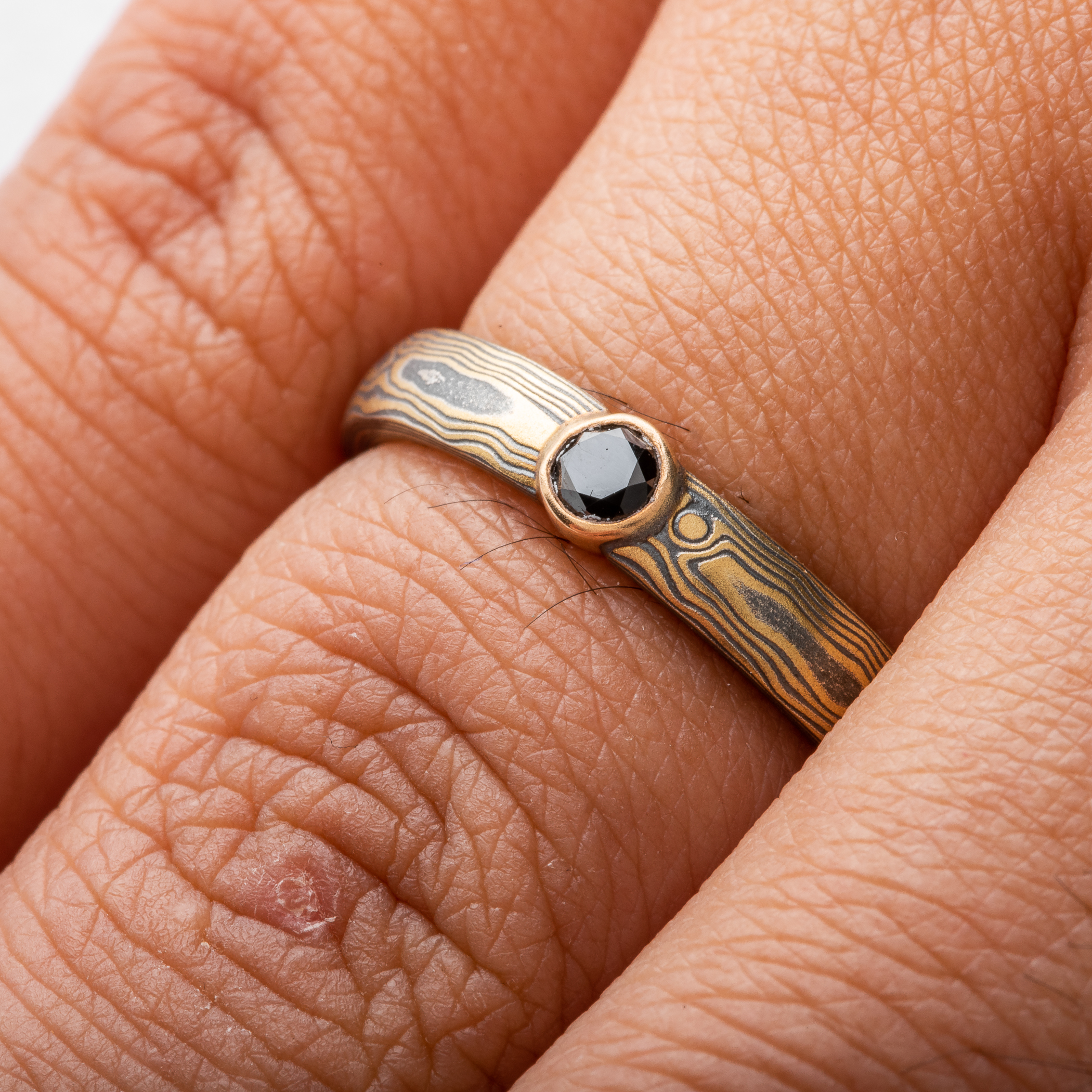 mokume gane ring by arn krebs in spark metal palette and woodgrain pattern with bezel set black diamond