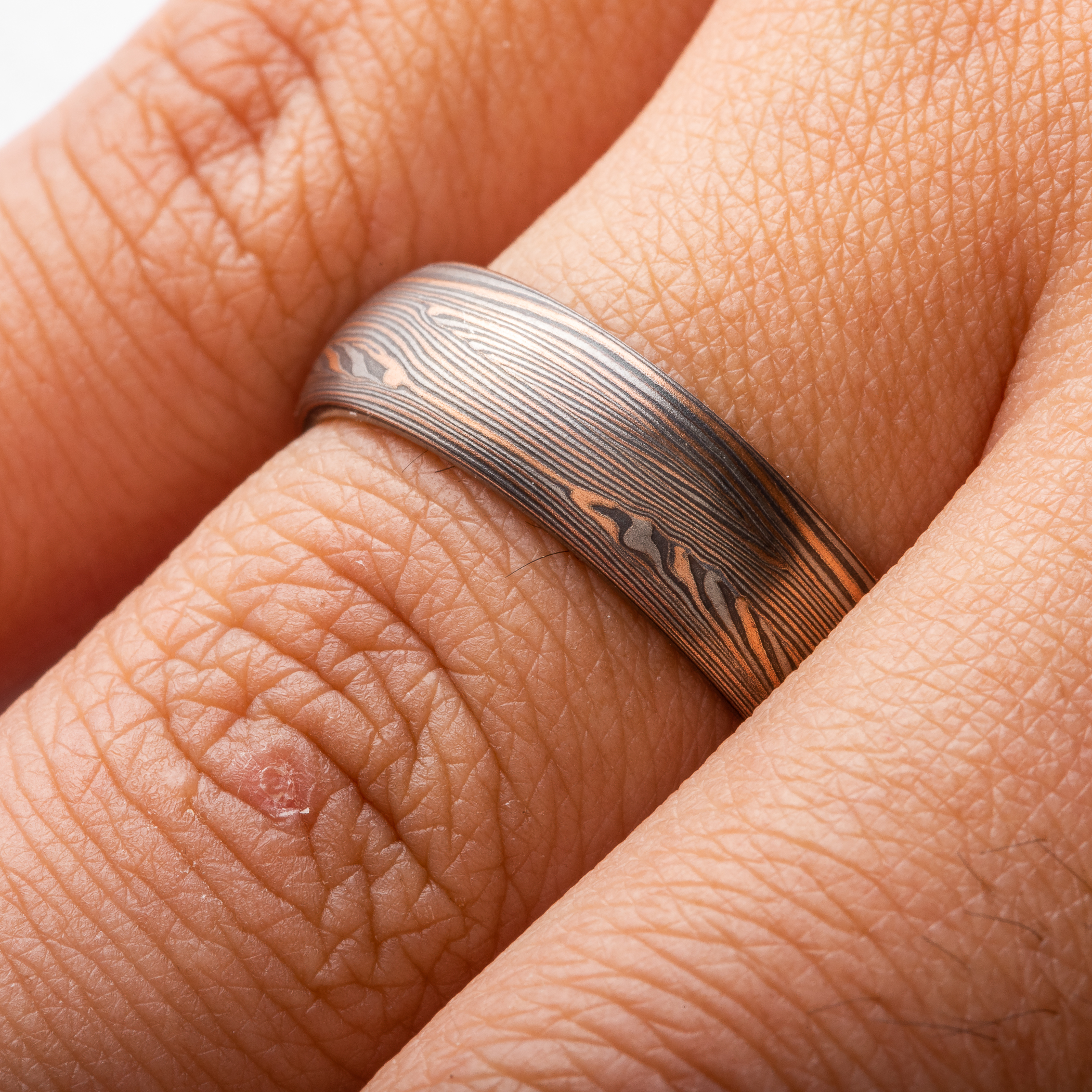 Warm toned mokume gane ring, patterned in a linear style with many layers of fine lines in alternating red gold, palladium and oxidized silver. Medium width band with a domed profile.