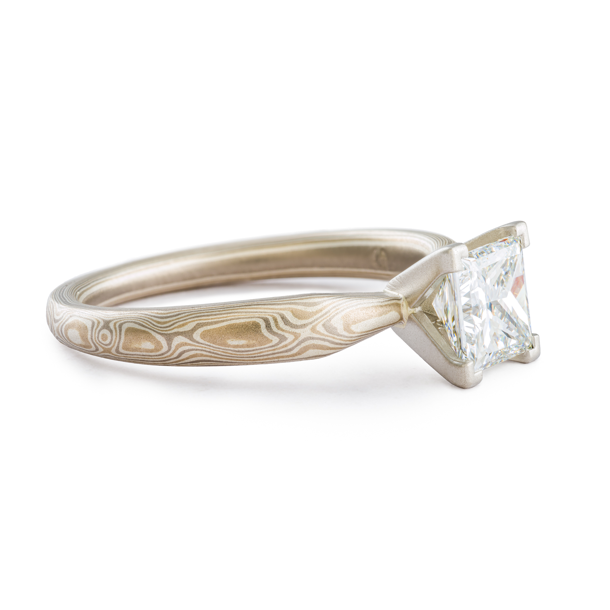solitaire style mokume gane engagement ring with square diamond set in prongs, ring has an overall silvery palette and a woodgrain style