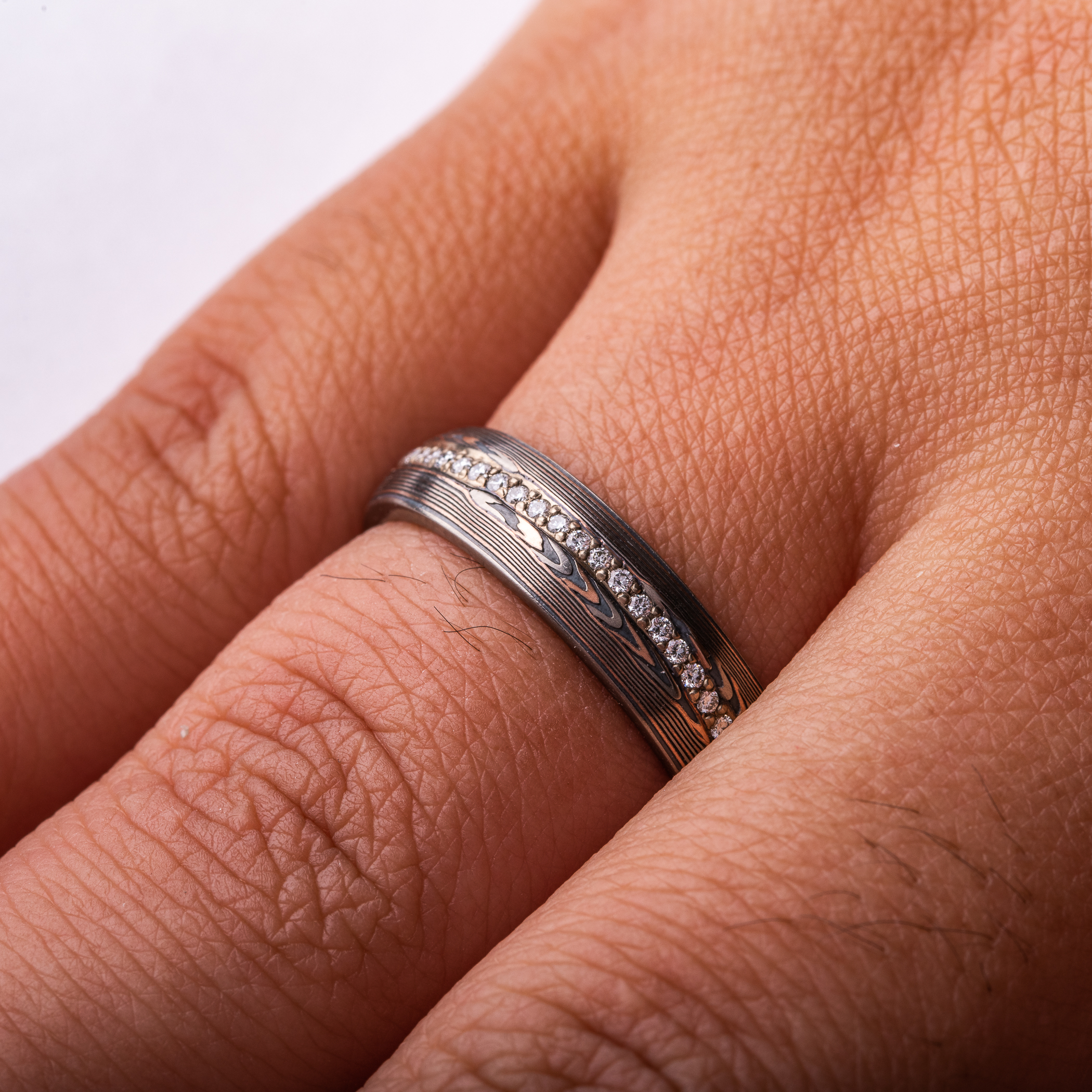 mokume gane patterned ring, red gold palladium and oxidized silver, with a line of diamonds set in the center of the band. The line gently curves around the patterning.
