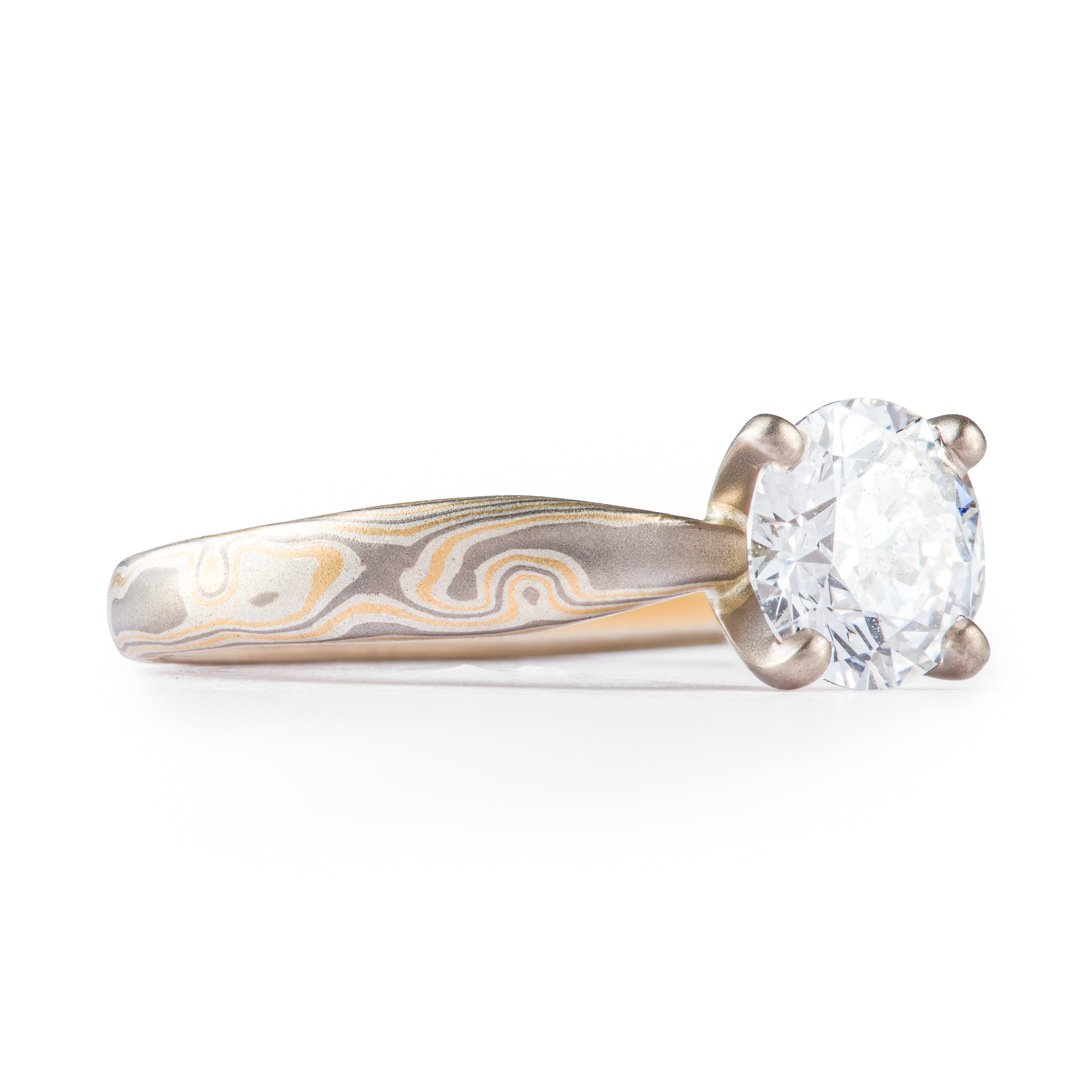 Arn Krebs mokume engagement ring, patterned in a woodgrain style with yellow gold and silver and gray metals, with a solitaire round diamond set in prongs.