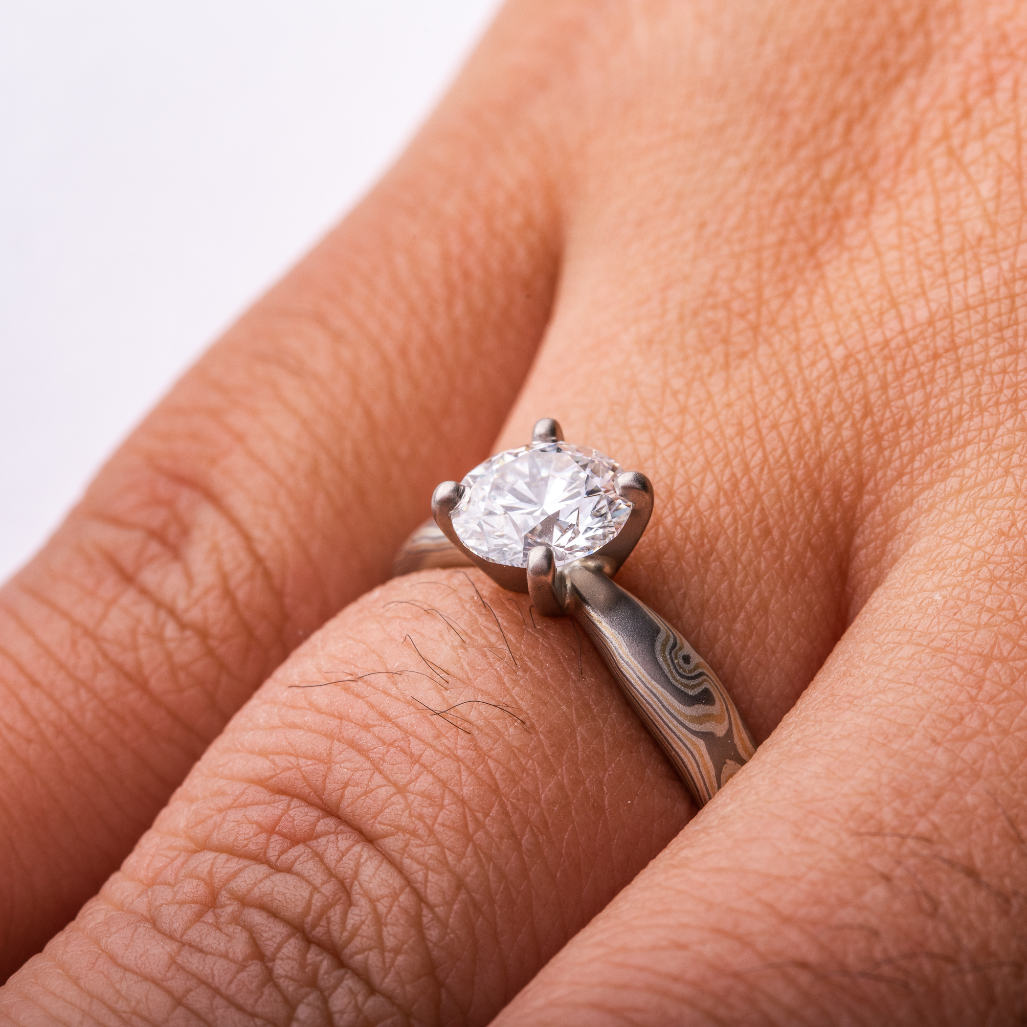 Arn Krebs mokume engagement ring, patterned in a woodgrain style with yellow gold and silver and gray metals, with a solitaire round diamond set in prongs.
