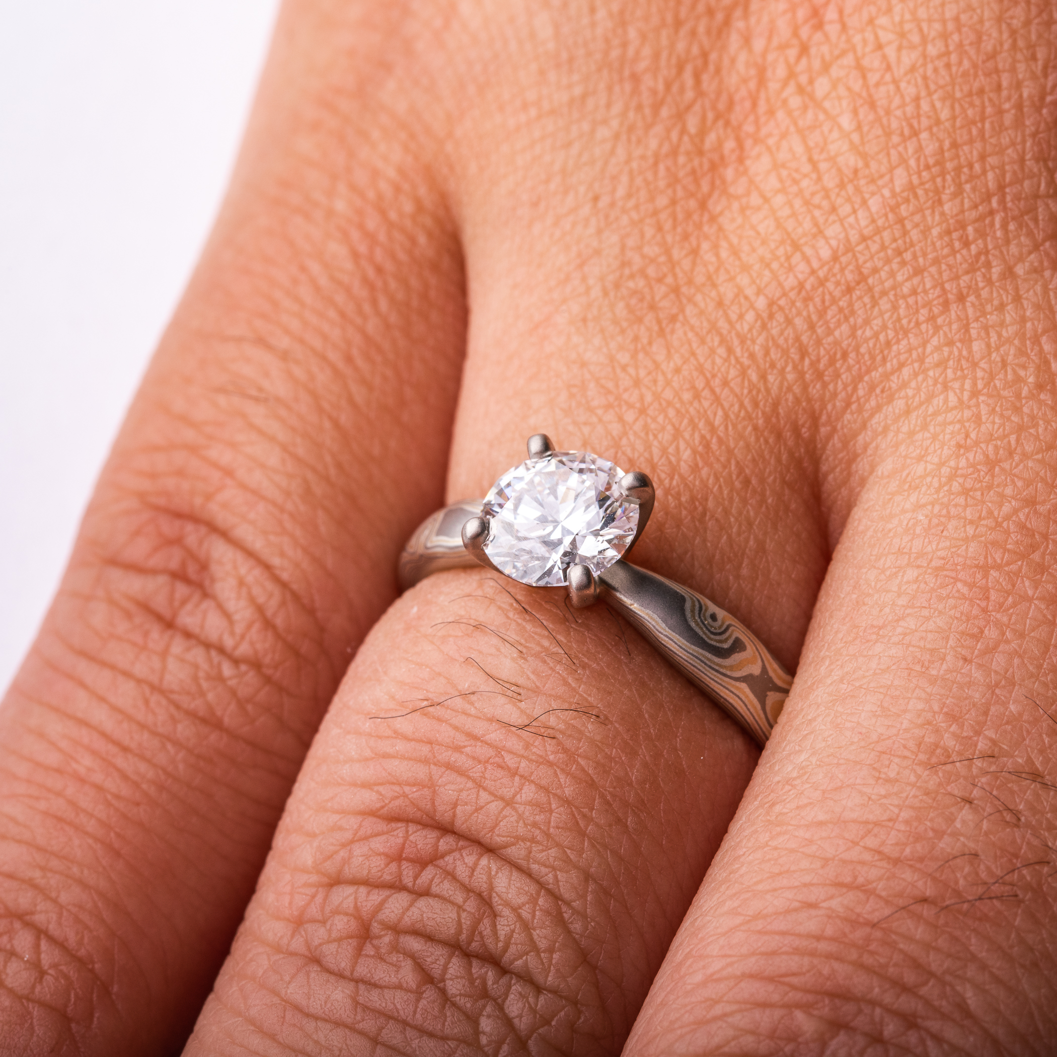 Arn Krebs mokume engagement ring, patterned in a woodgrain style with yellow gold and silver and gray metals, with a solitaire round diamond set in prongs.