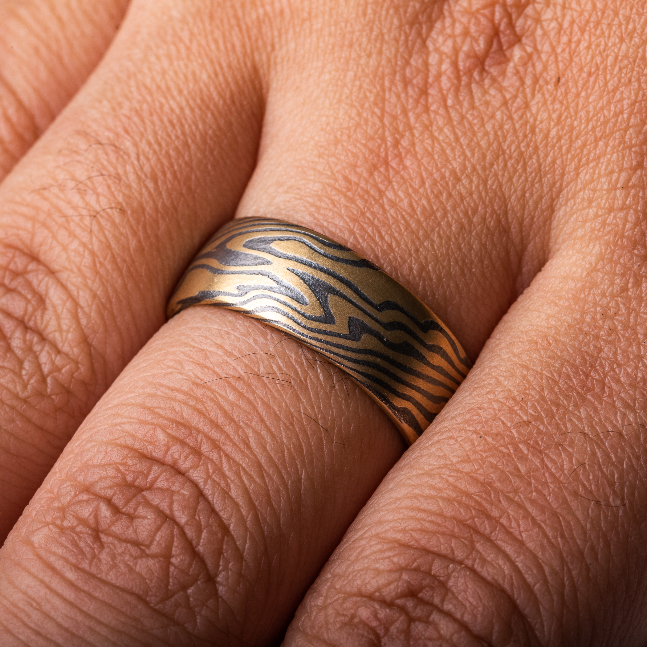 Wide men's style mokume gane ring made with layers of yellow gold and oxidized silver (black), in a dynamic twisting pattern.