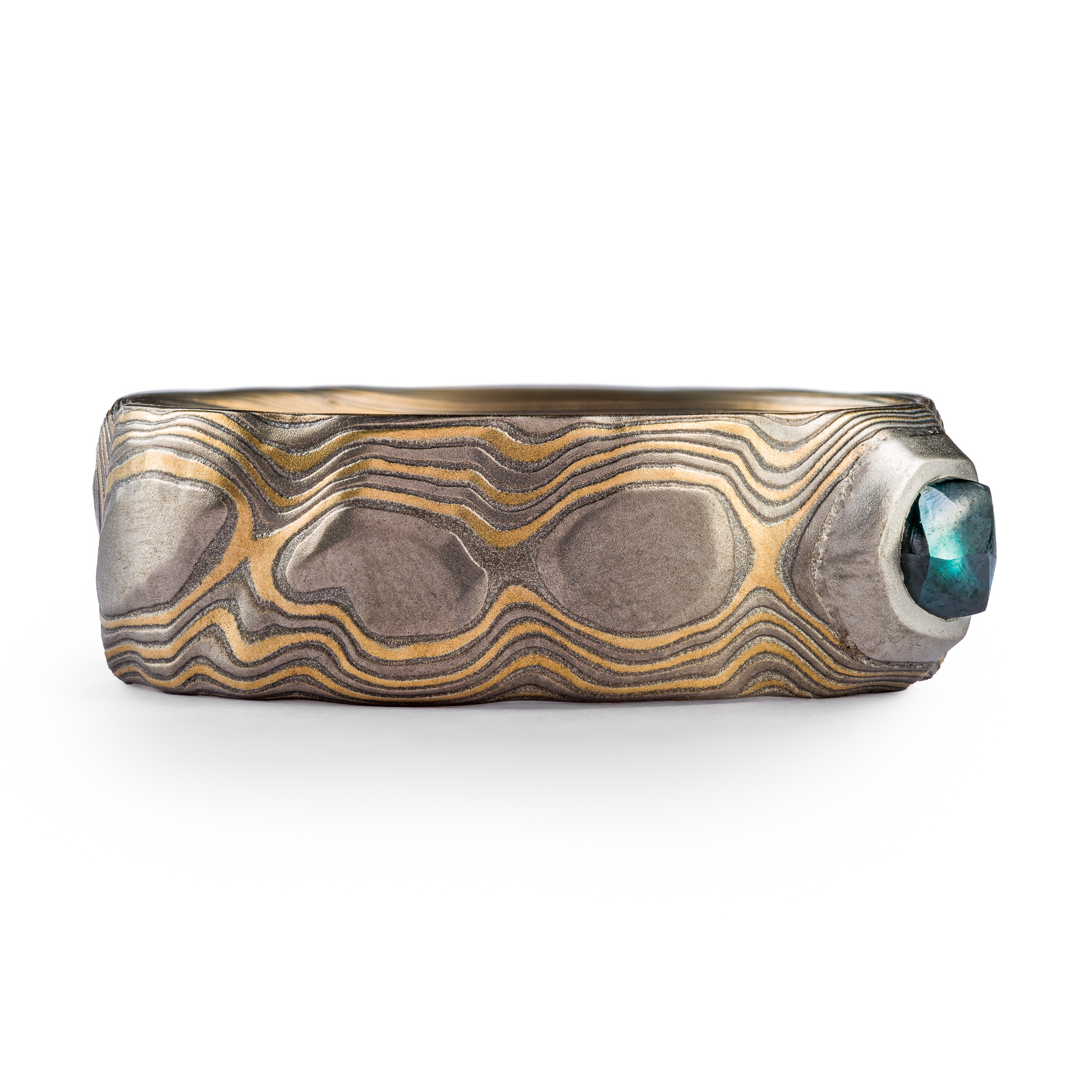 Wide men's style mokume gane ring carved to look like rocks, with a blue diamond crystal set into it, looking like it's emerging from the earth.