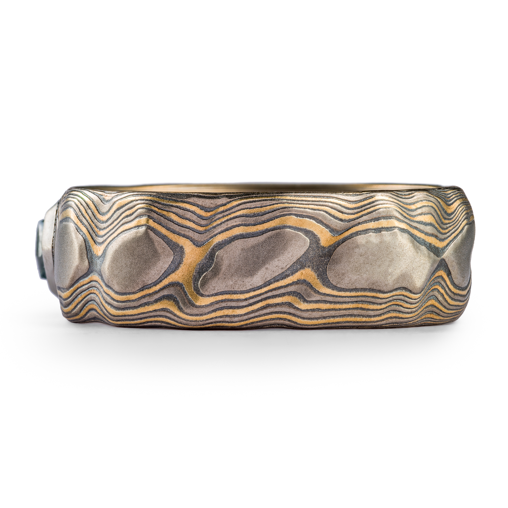 Wide men's style mokume gane ring carved to look like rocks, with a blue diamond crystal set into it, looking like it's emerging from the earth.