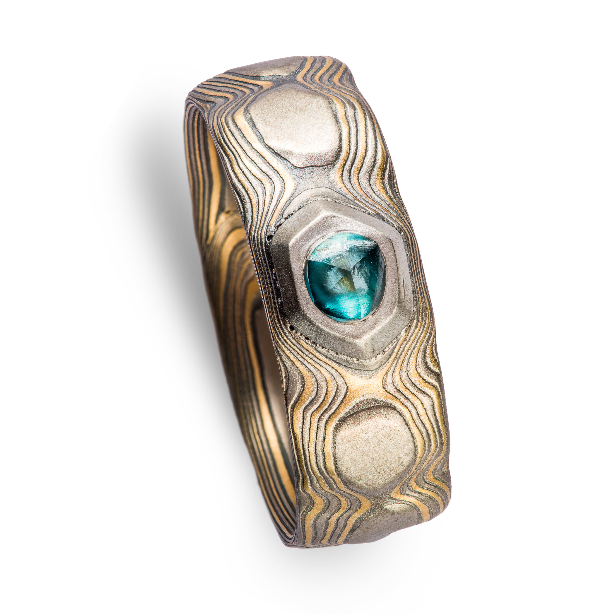 Wide men's style mokume gane ring carved to look like rocks, with a blue diamond crystal set into it, looking like it's emerging from the earth.