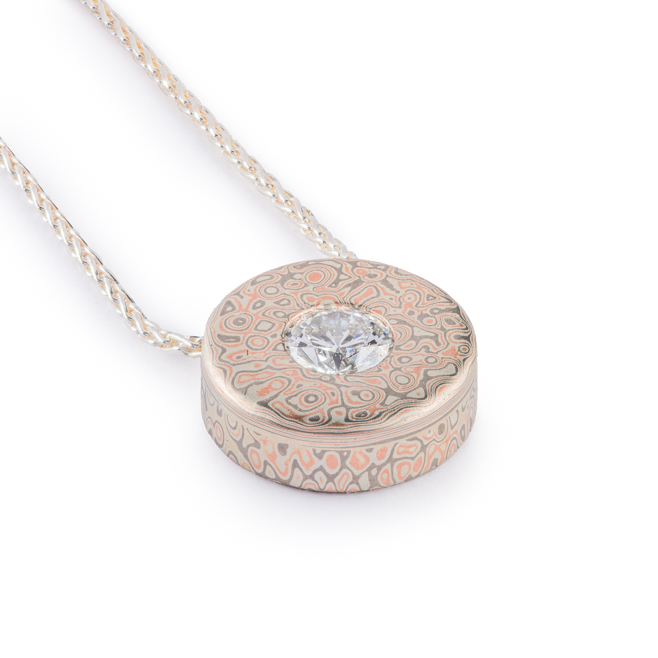 Small round pendant with a moissanite set in the center on a chain, patterned in a style that looks like raindrops on water.