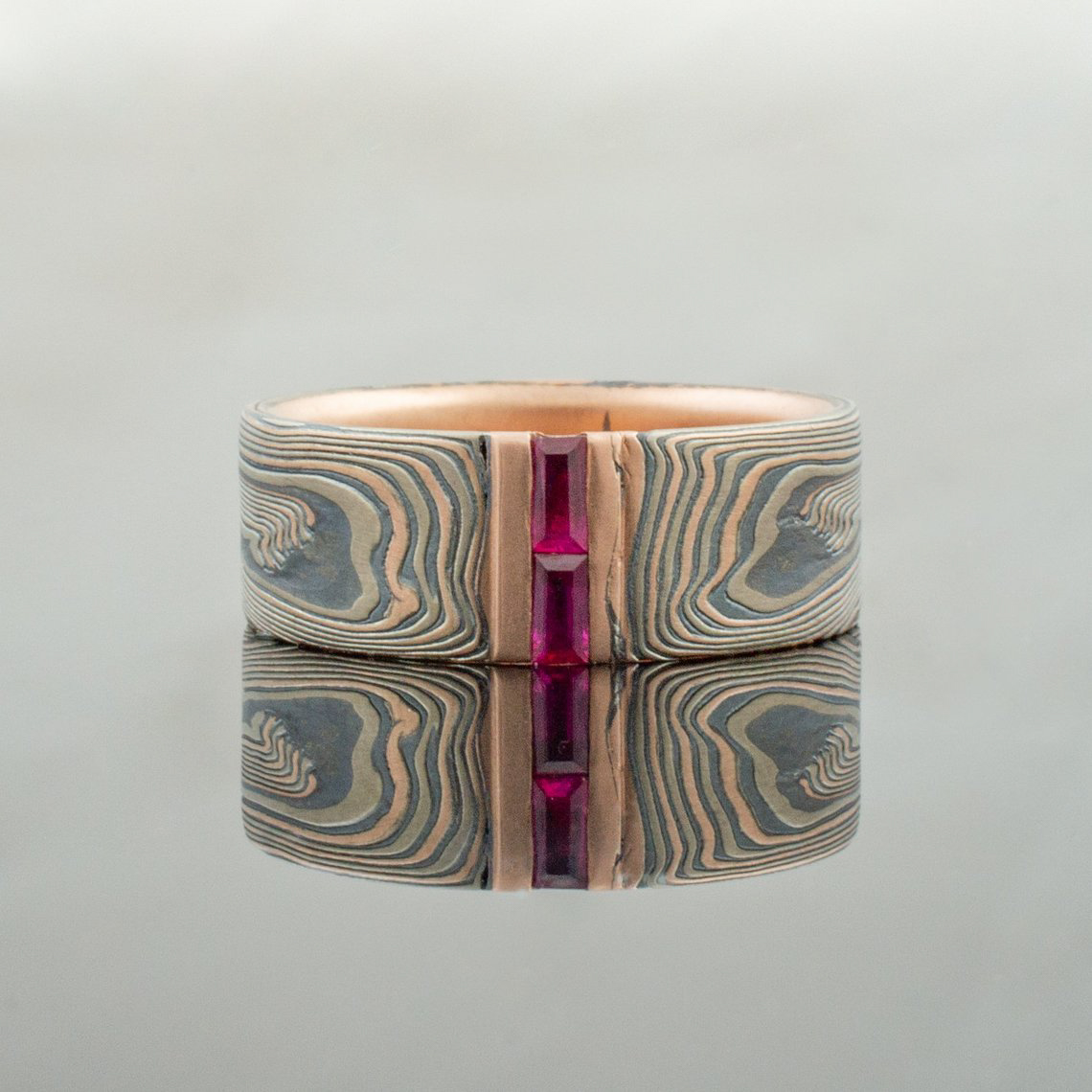 Mokume gane ring with red baguette stones set into the band, flat profile, made with red gold, palladium and silver.