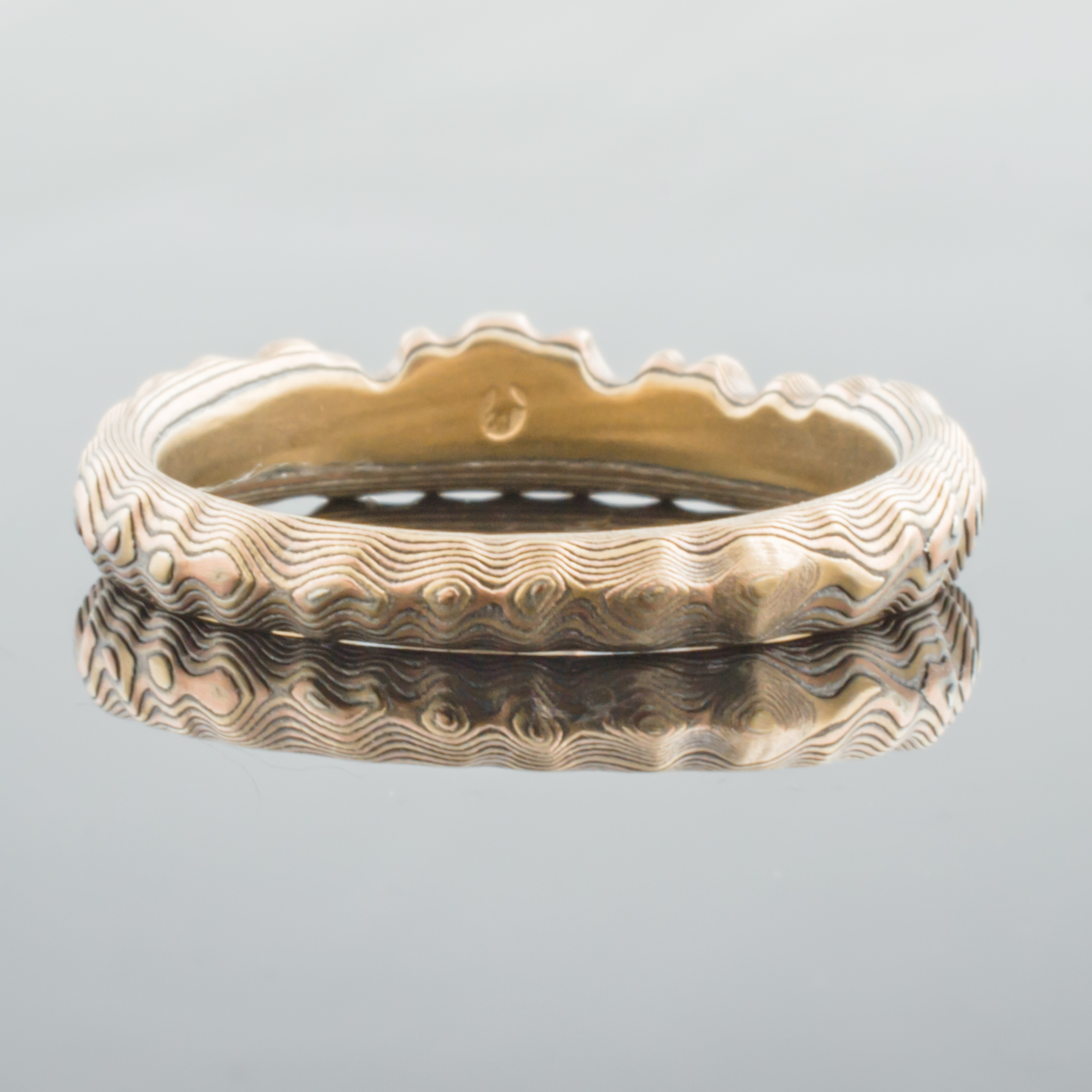 Uniquely contoured mokume gane ring with a shaped edge made to fit with an engagement ring, and textured to look like topography.