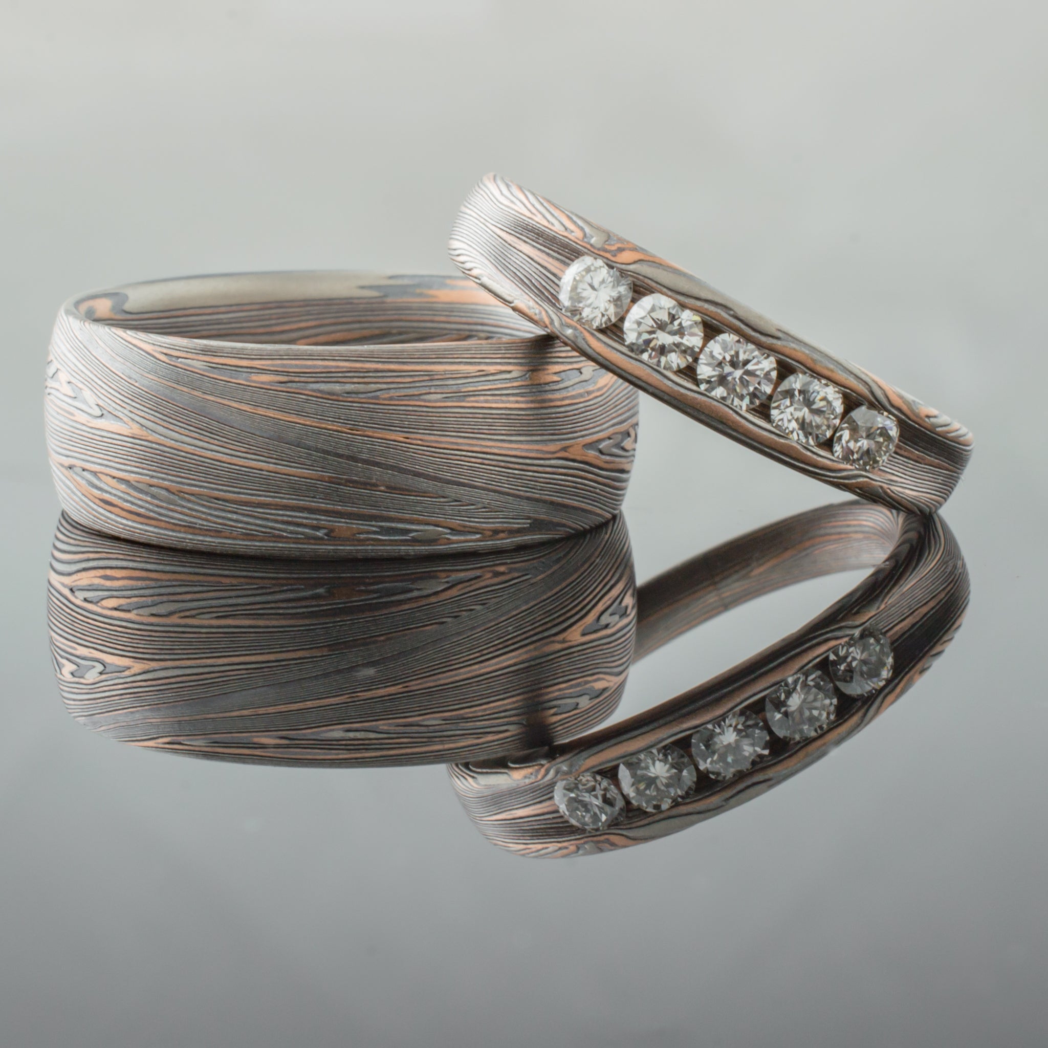 Matching mokume patterned wedding ring set, one ring with five diamonds set into it.