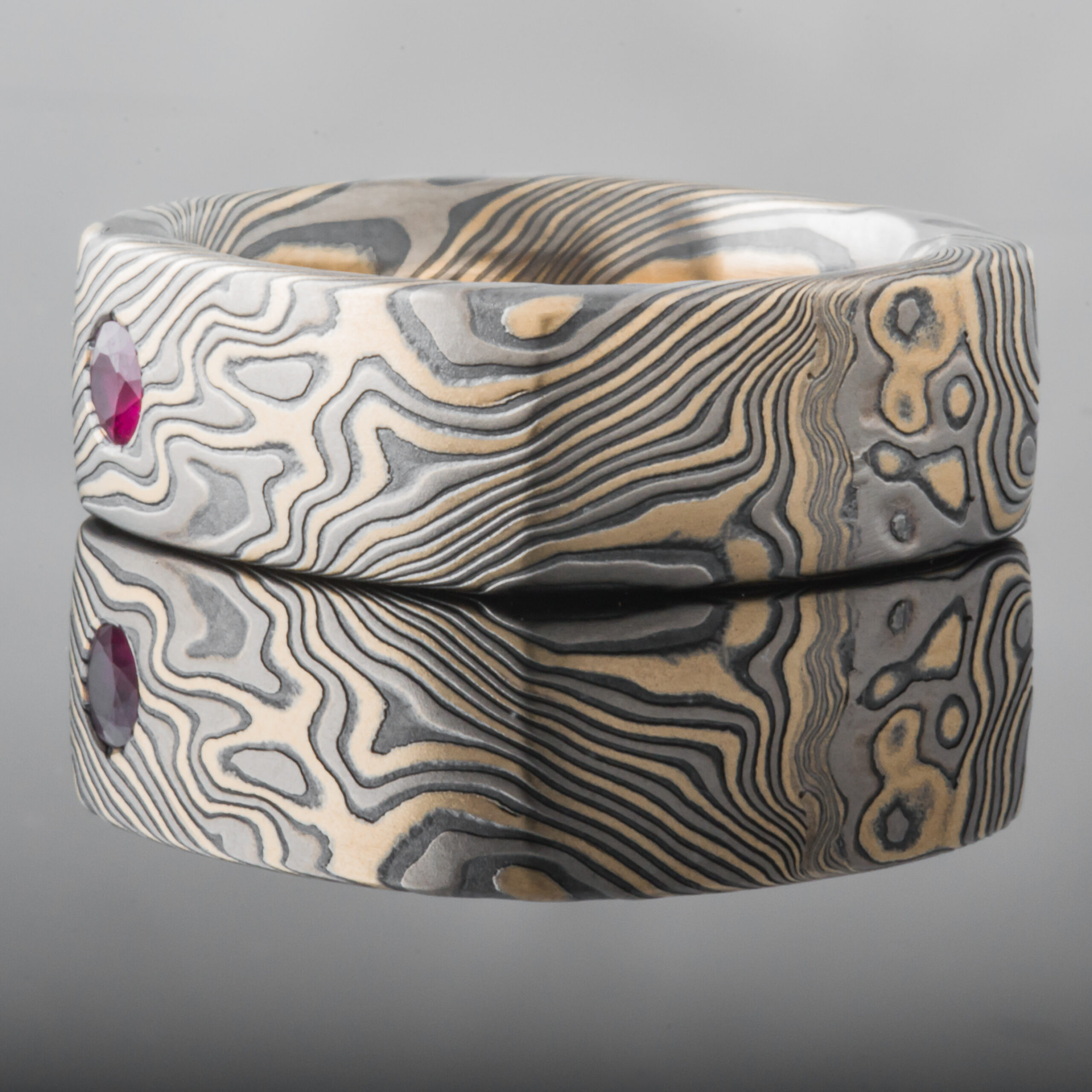 Wide rustic men's style square mokume gane ring made with yellow gold, palladium and oxidized silver, with a round white stone flush set into the band.