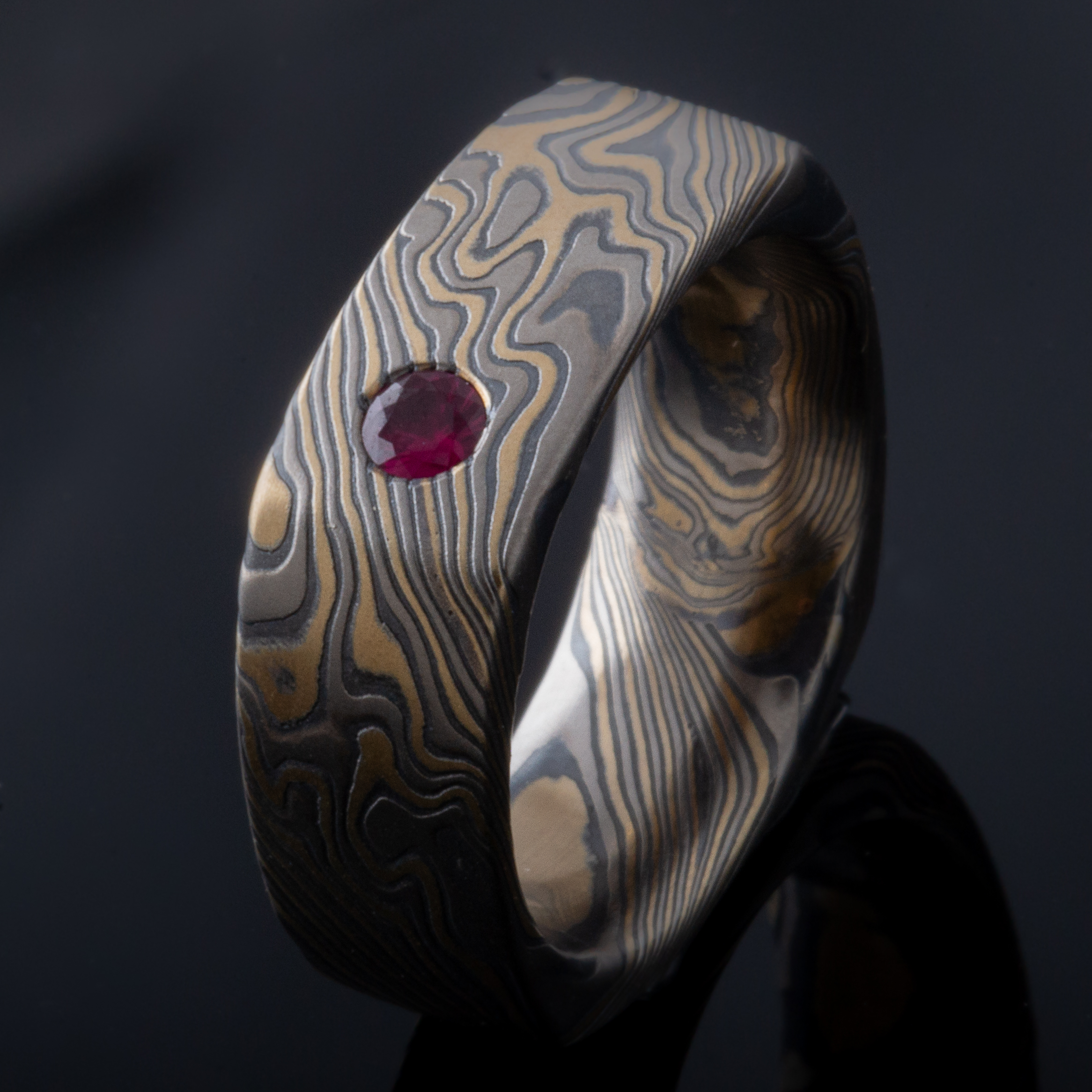 Wide rustic men's style square mokume gane ring made with yellow gold, palladium and oxidized silver, with a round white stone flush set into the band.