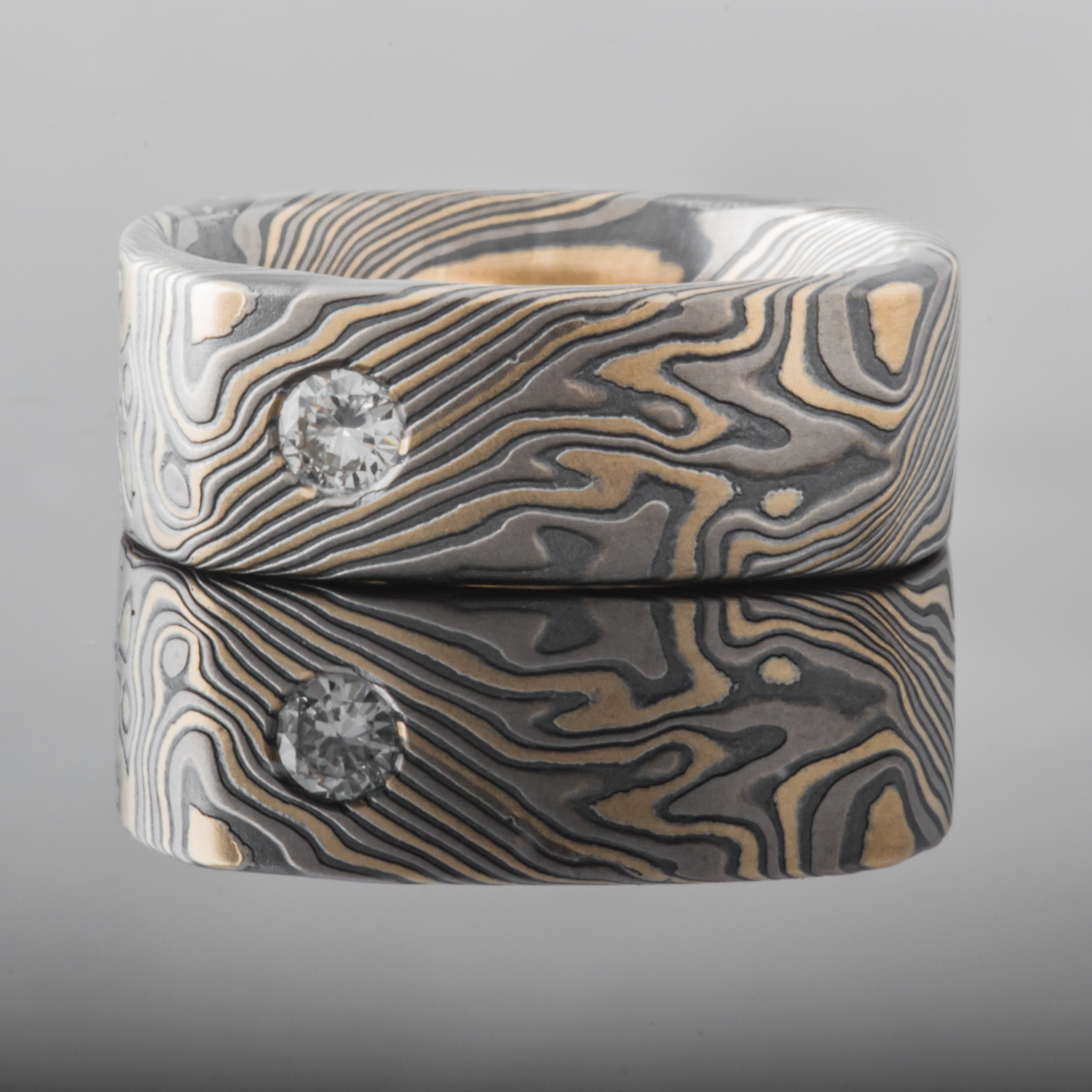 Wide rustic men's style square mokume gane ring made with yellow gold, palladium and oxidized silver, with a round white stone flush set into the band.