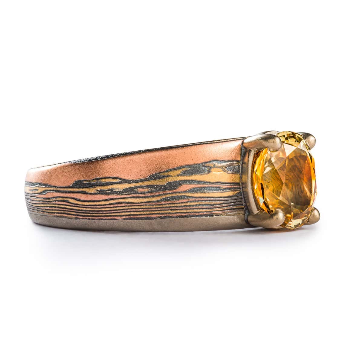 unique tapered ring with a large orange sapphire set into it, band is made to look like a landscape, a sunset at a beach with dark clouds