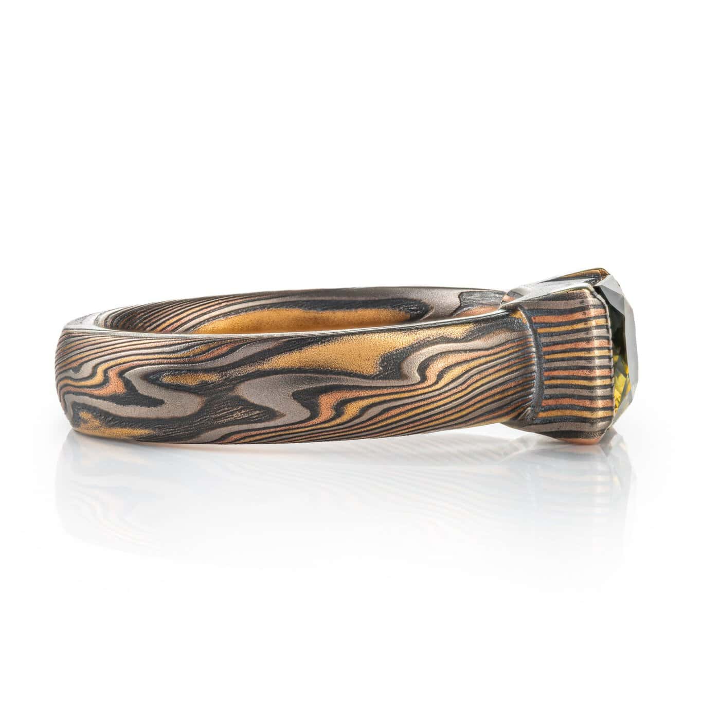 engagement style ring featuring a large rectangular australian sapphire shown in a mossy green with yellow highlights, paired with an earthy metal combination of red and yellow golds, palladium and oxidized silver