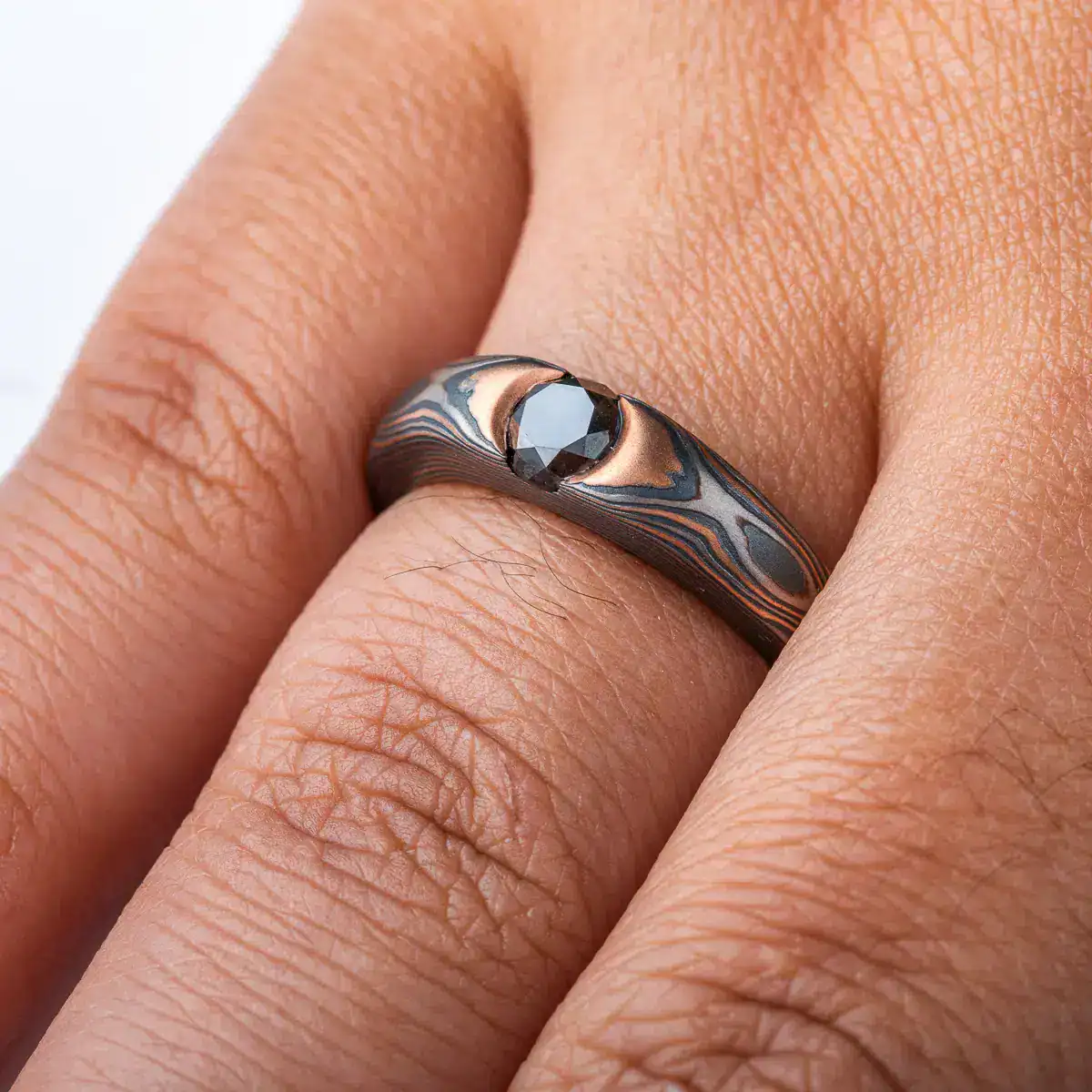 dark and moody feeling mokume gane ring, with solitaire black diamond in cathedral style setting, metals in the ring are red gold, palladium and oxidized silver