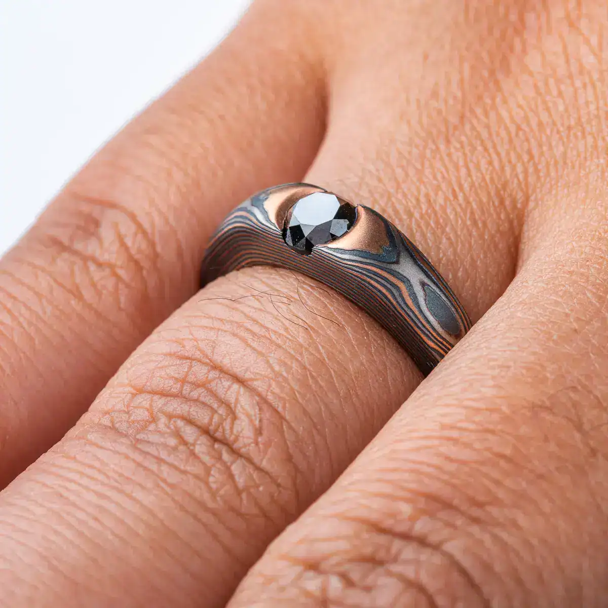 dark and moody feeling mokume gane ring, with solitaire black diamond in cathedral style setting, metals in the ring are red gold, palladium and oxidized silver