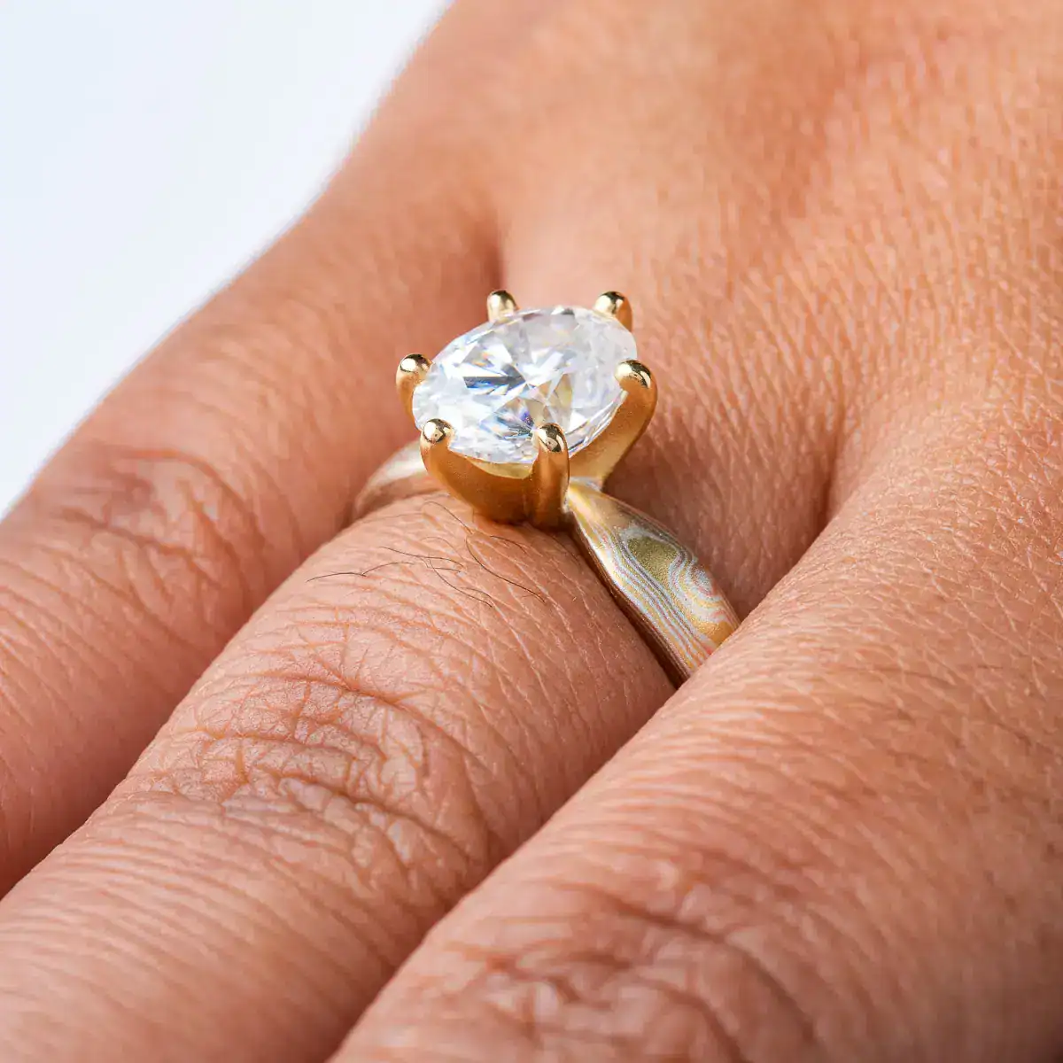 elegant six prong style engagement ring with an oval shaped diamond, band is woodgrain patterned and made in 18kt gold