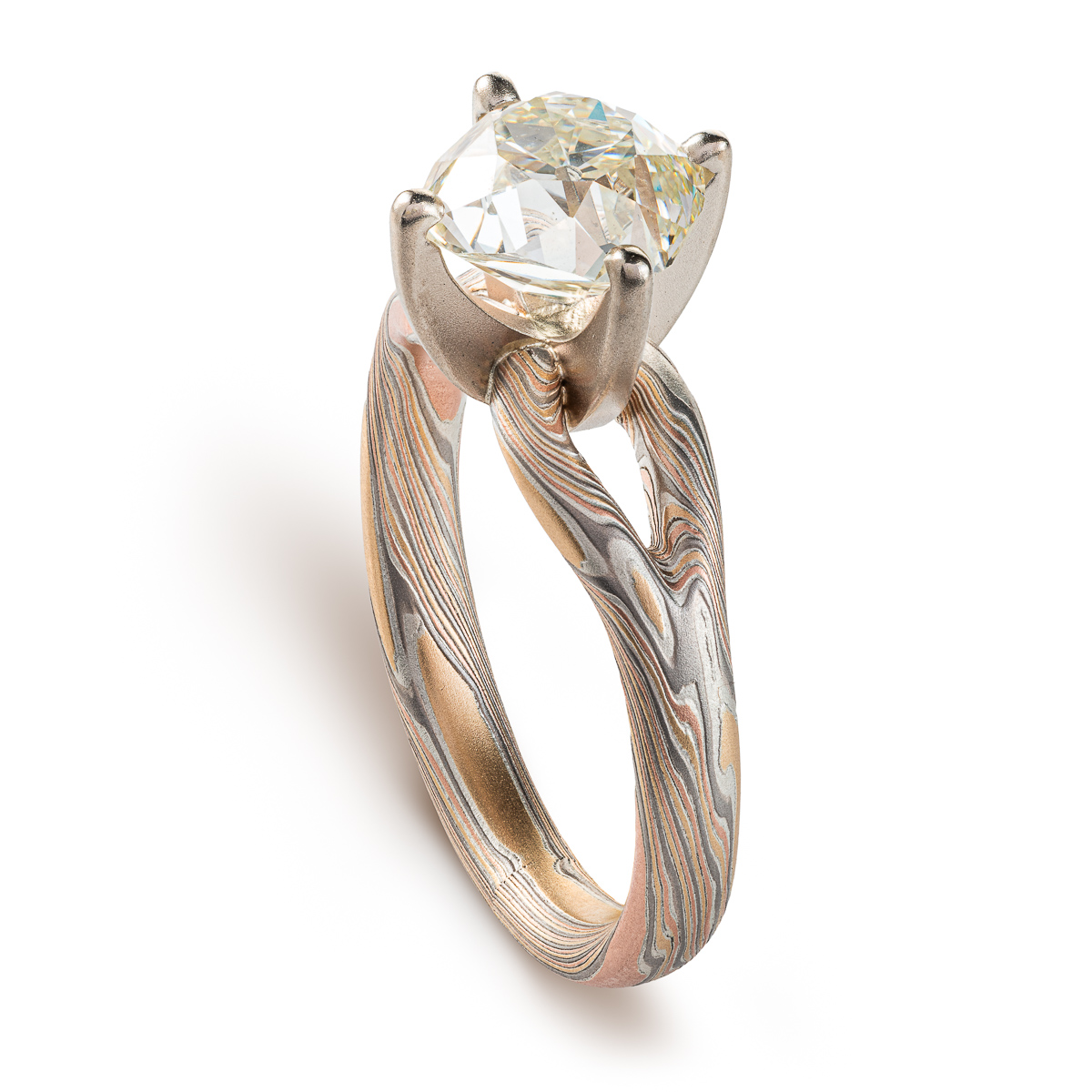 mokume ring with large cushion shaped diamond held in prongs, the band part of the ring is split into a y shape leading into the stone on either side