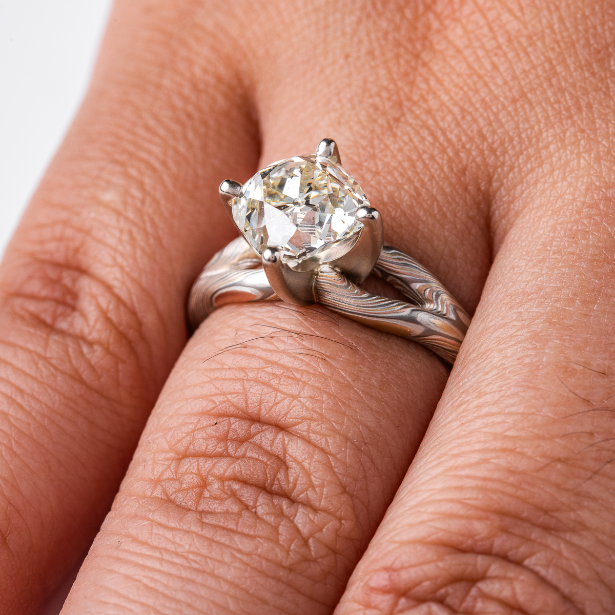 mokume ring with large cushion shaped diamond held in prongs, the band part of the ring is split into a y shape leading into the stone on either side