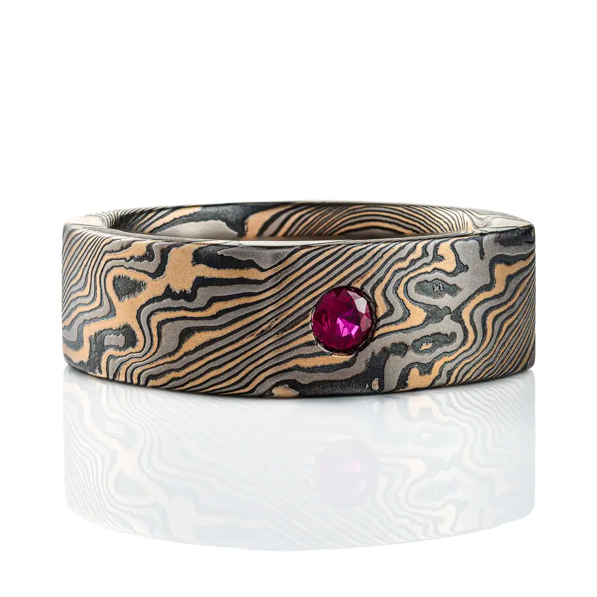 uniquely shaped mokume gane band with a soft square shape on the outside (inside is still circular), with a flat profile for a modern look, and two small stones set flush into the surface, one white and one red.