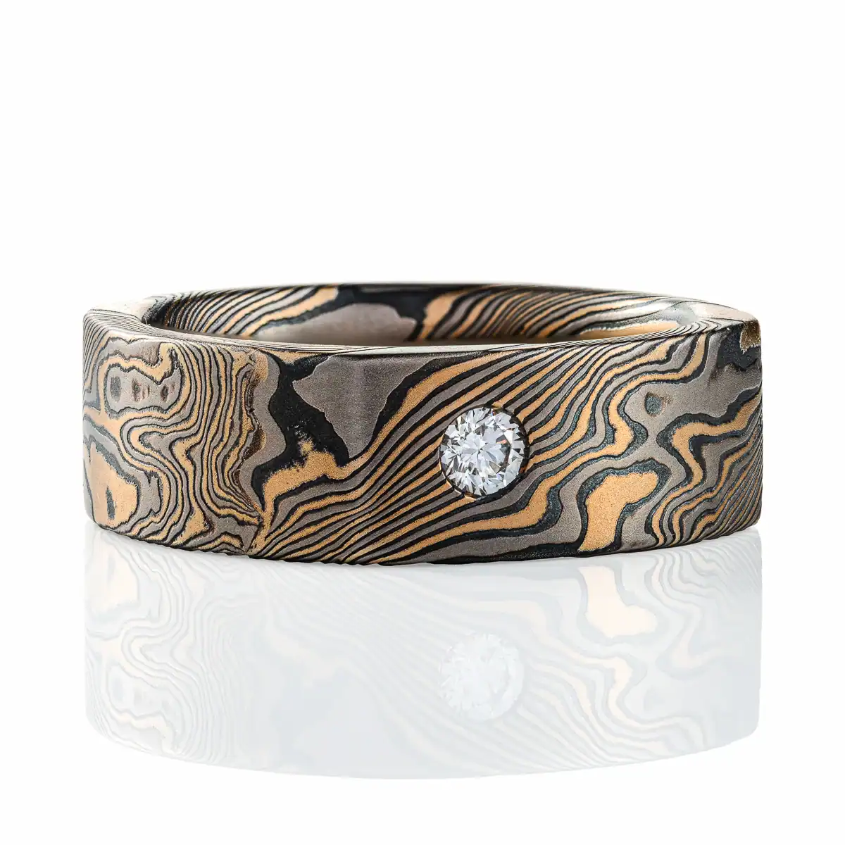 uniquely shaped mokume gane band with a soft square shape on the outside (inside is still circular), with a flat profile for a modern look, and two small stones set flush into the surface, one white and one red.