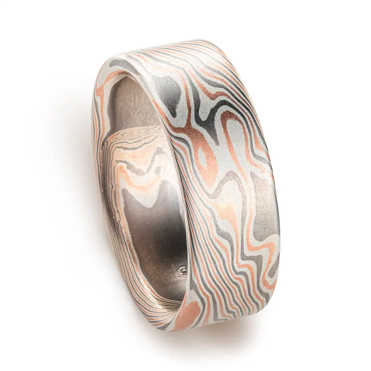 Large, wide mokume ring with bold twist style patterning running diagonally across, with a flat profile and smooth finish. Made with alternating layers of red gold, silver and palladium.