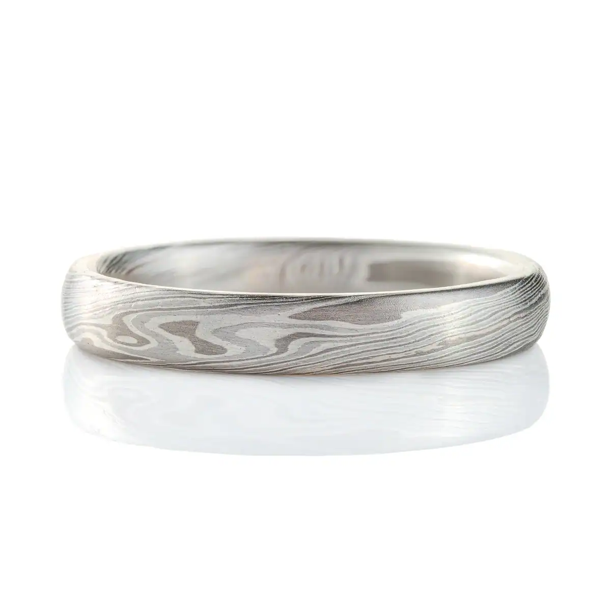 mokume gane band in silvery palette with different shades of gray, made in a twisting pattern and a smooth finish.