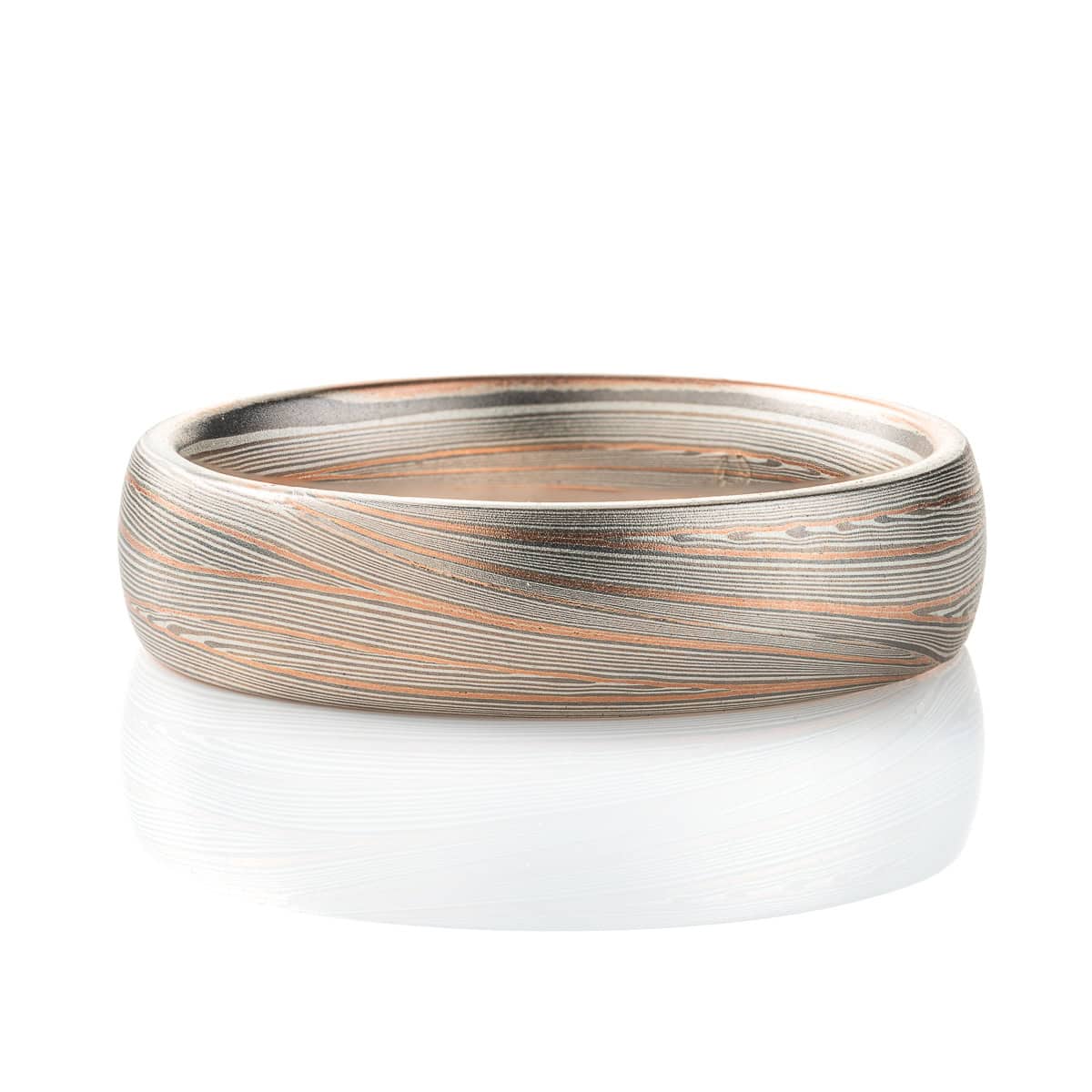 Domed band patterned in mokume style with long thin lines flowing around the ring, made of layers of light and darker gray silver metal, with two layers of red gold added. .