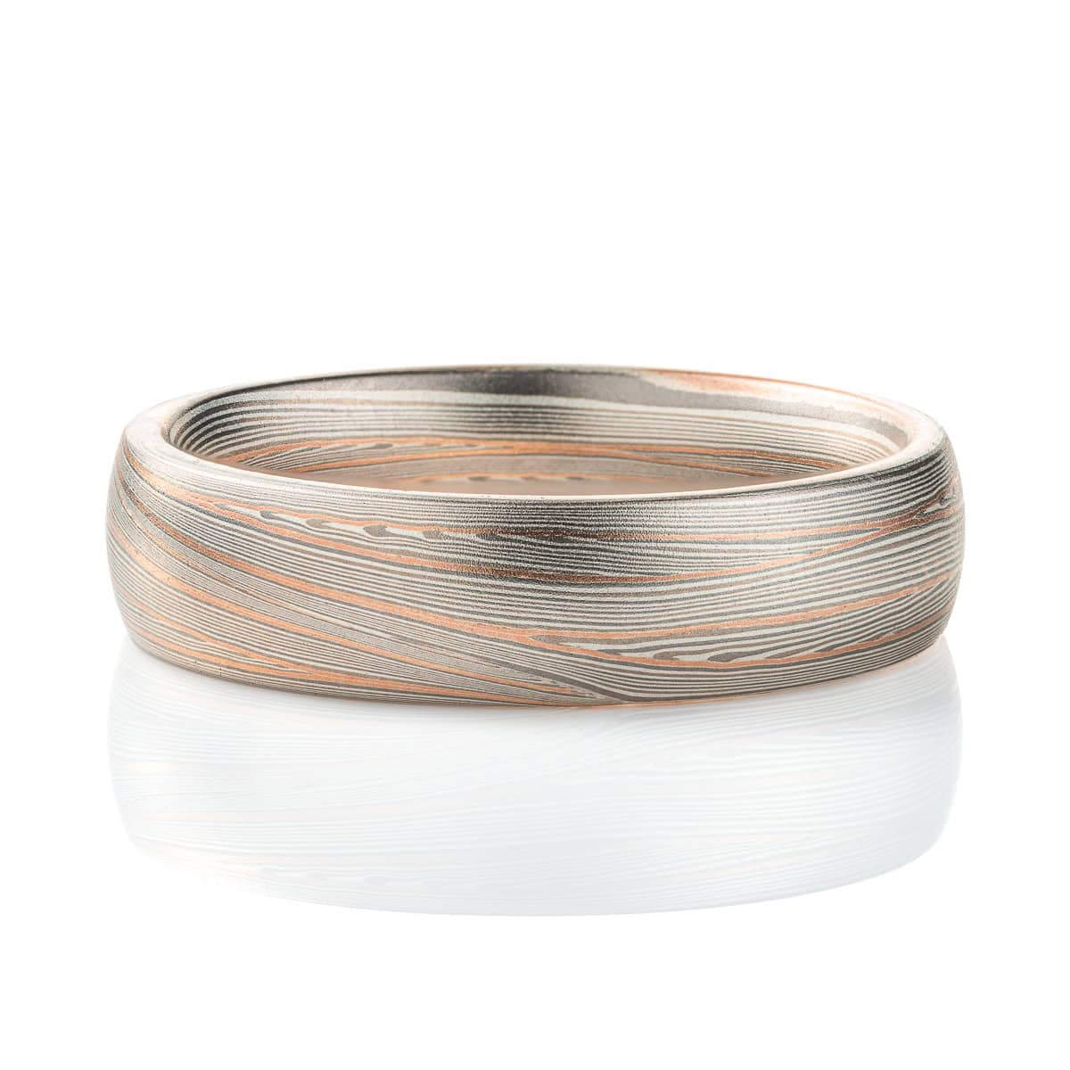 Domed band patterned in mokume style with long thin lines flowing around the ring, made of layers of light and darker gray silver metal, with two layers of red gold added. .