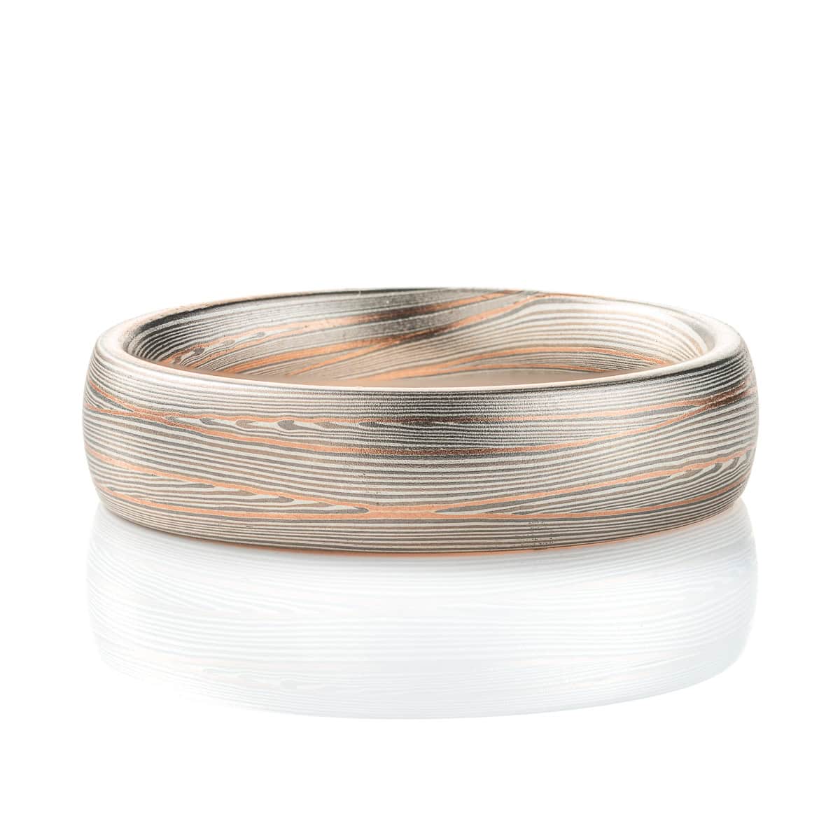 Domed band patterned in mokume style with long thin lines flowing around the ring, made of layers of light and darker gray silver metal, with two layers of red gold added.