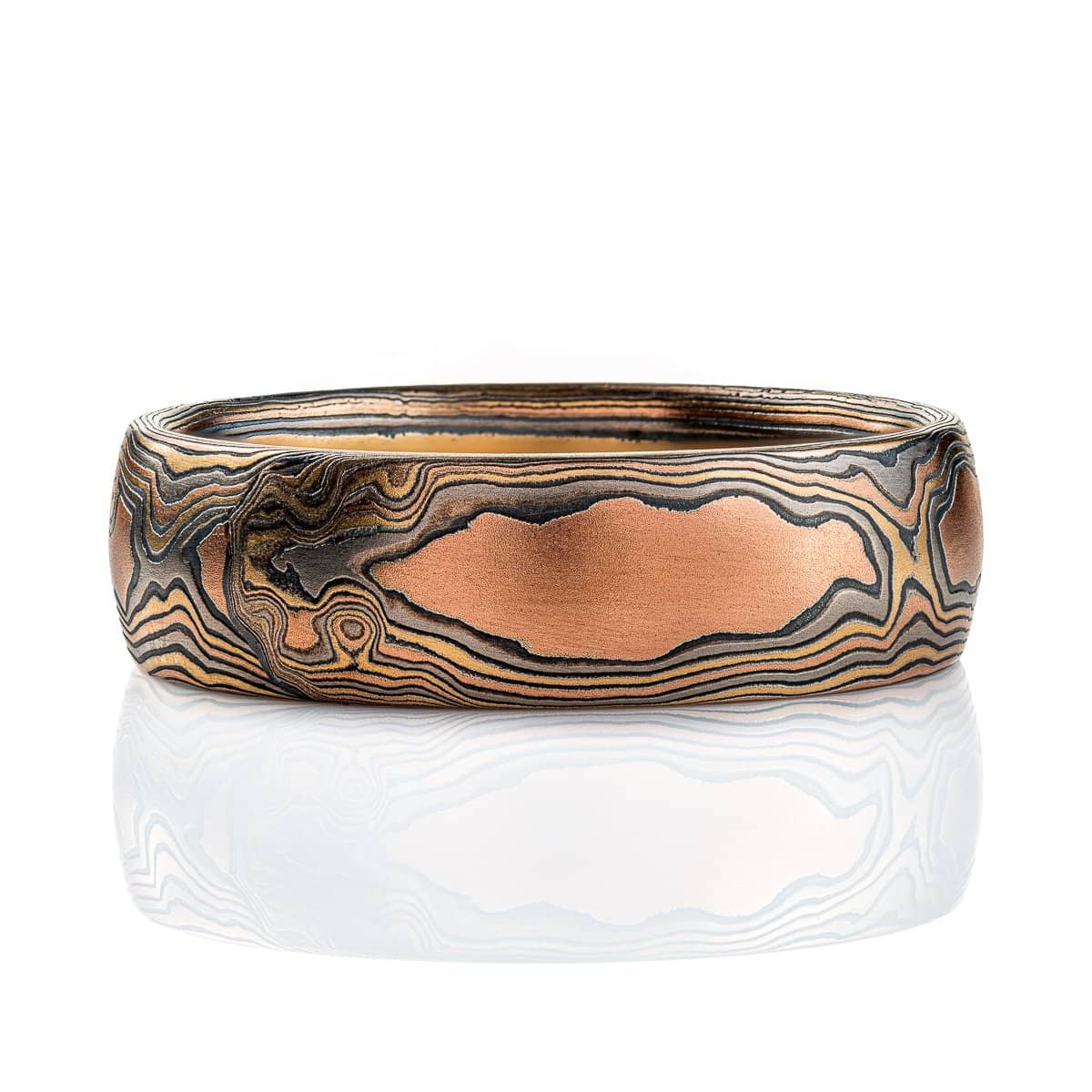 Wide men's style mokume gane band with a domed profile, made in a woodgrain style pattern to resemble wood, with layers of red gold and yellow gold alternating with oxidized silver (black).
