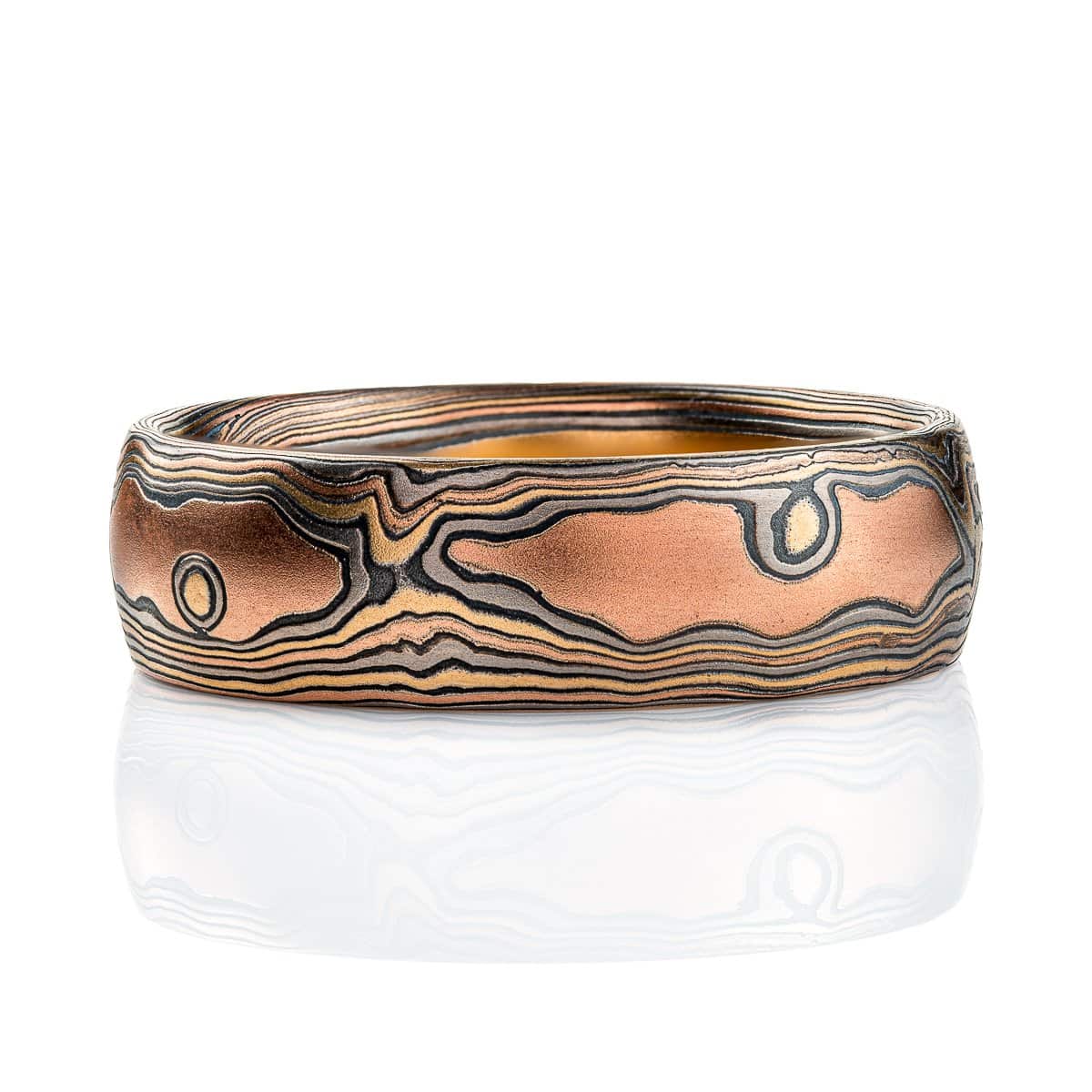 Wide men's style mokume gane band with a domed profile, made in a woodgrain style pattern to resemble wood, with layers of red gold and yellow gold alternating with oxidized silver (black).