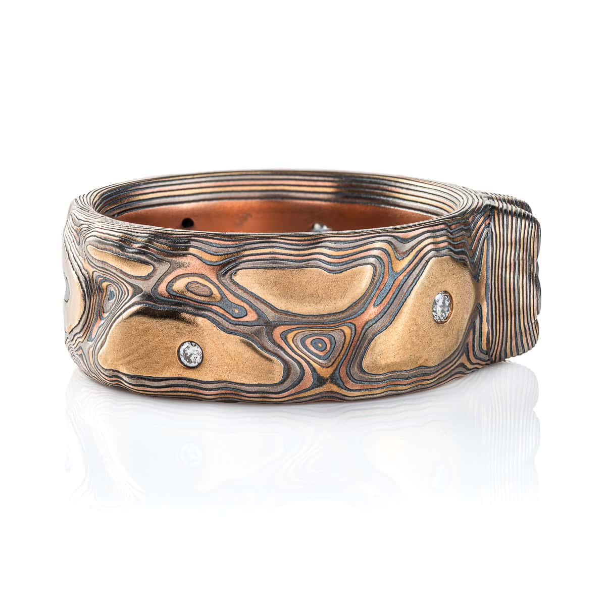 Large men's style mokume gane patterned ring, made to resemble rock formations and mountains, with a large dark blue and orange stone set into the ring in a raised area, intended to look like it's being excavated from the earth.