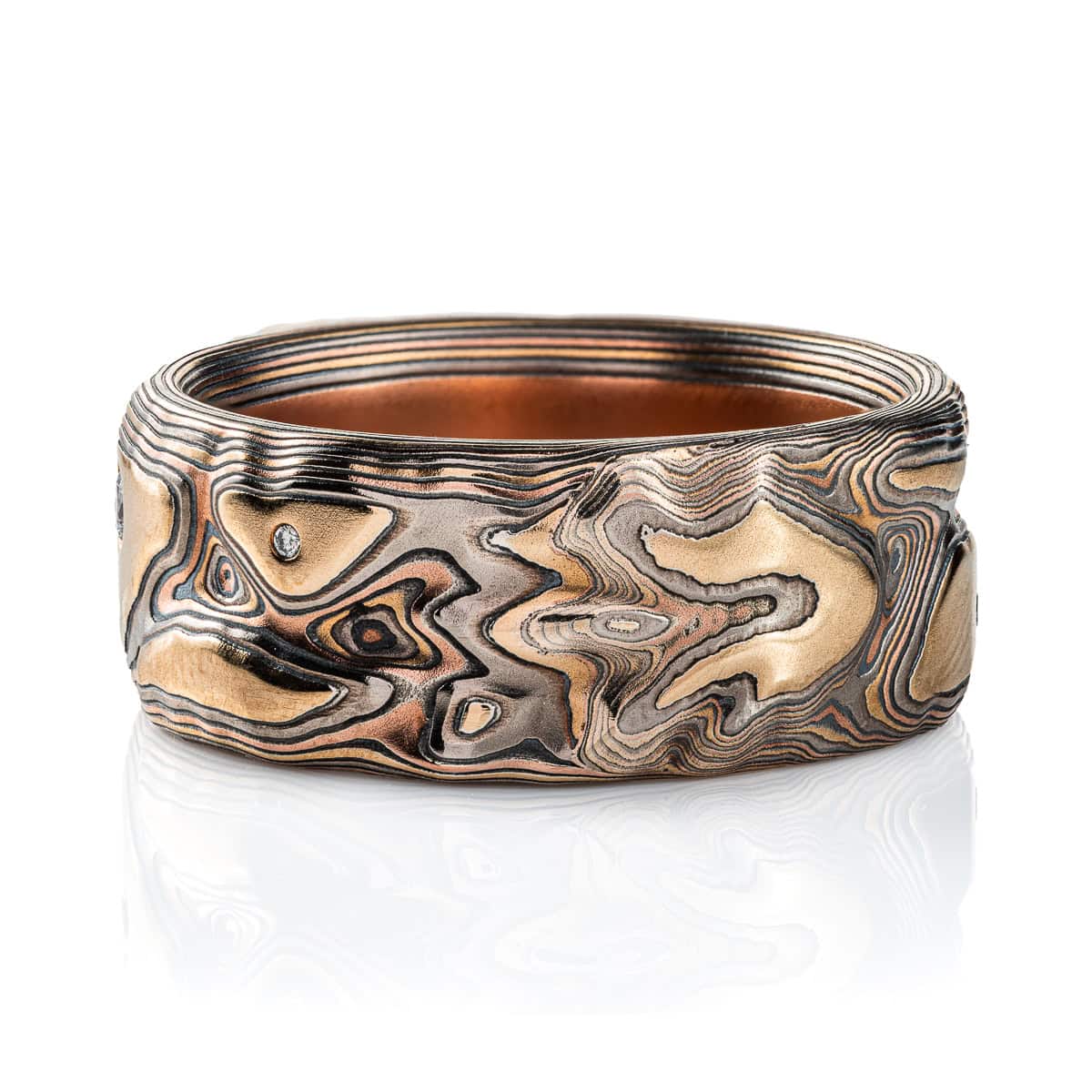 Large men's style mokume gane patterned ring, made to resemble rock formations and mountains, with a large dark blue and orange stone set into the ring in a raised area, intended to look like it's being excavated from the earth.