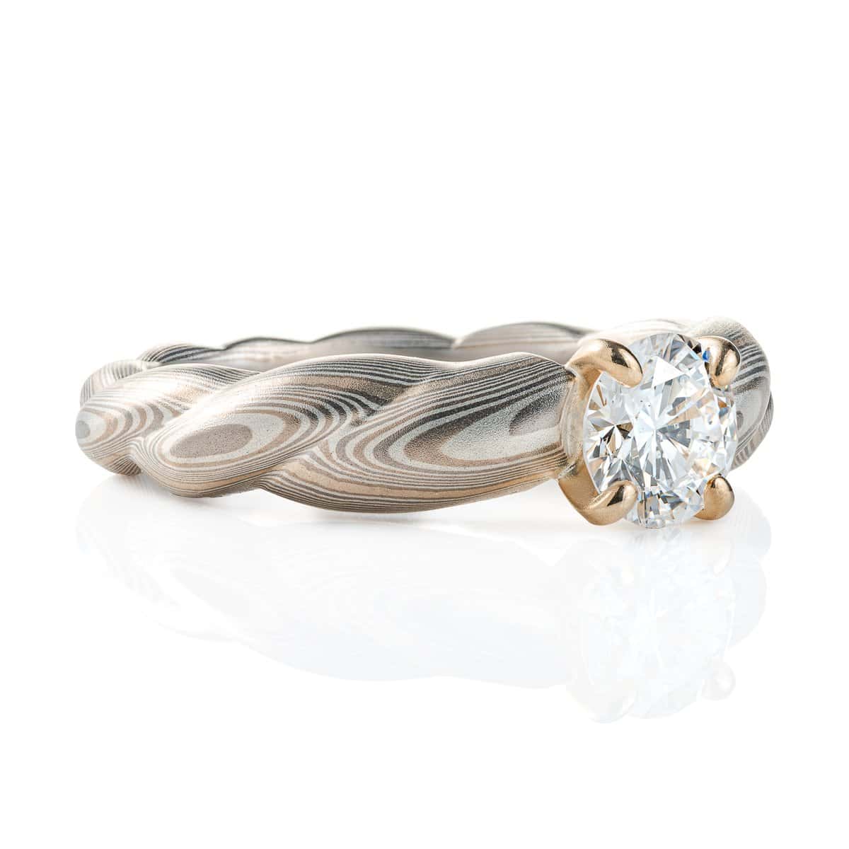 Mokume gane patterned engagement ring, carved to look like twisted rope, with a round diamond set into prongs at the top of the ring.