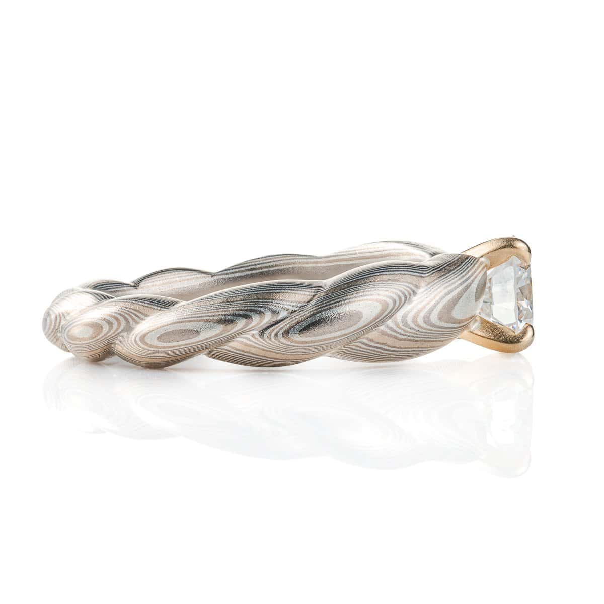 Mokume gane patterned engagement ring, carved to look like twisted rope, with a round diamond set into prongs at the top of the ring.