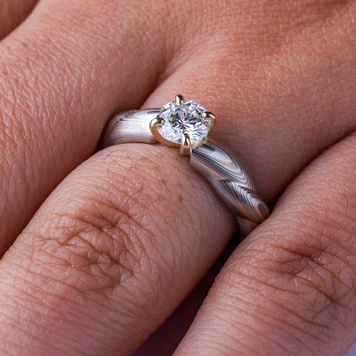 Mokume gane patterned engagement ring, carved to look like twisted rope, with a round diamond set into prongs at the top of the ring.