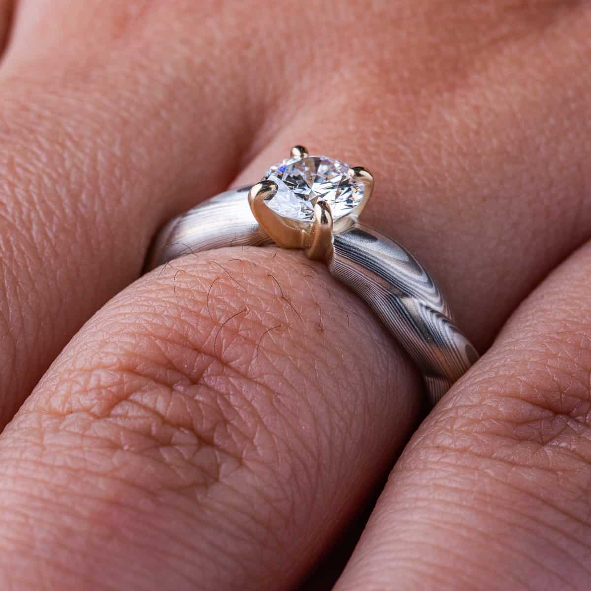Mokume gane patterned engagement ring, carved to look like twisted rope, with a round diamond set into prongs at the top of the ring.