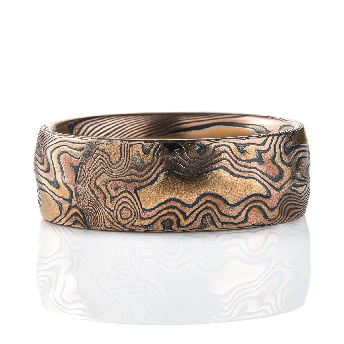 Wide mokume gane patterned ring, made with red and yellow gold and oxidized silver, with added carving to create a rippling, textured effect.
