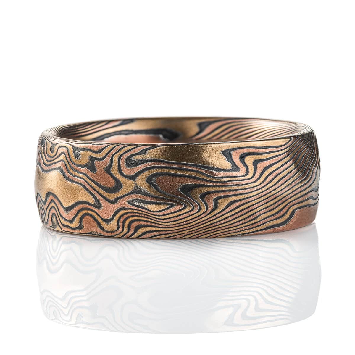 Wide mokume gane patterned ring, made with red and yellow gold and oxidized silver, with added carving to create a rippling, textured effect.