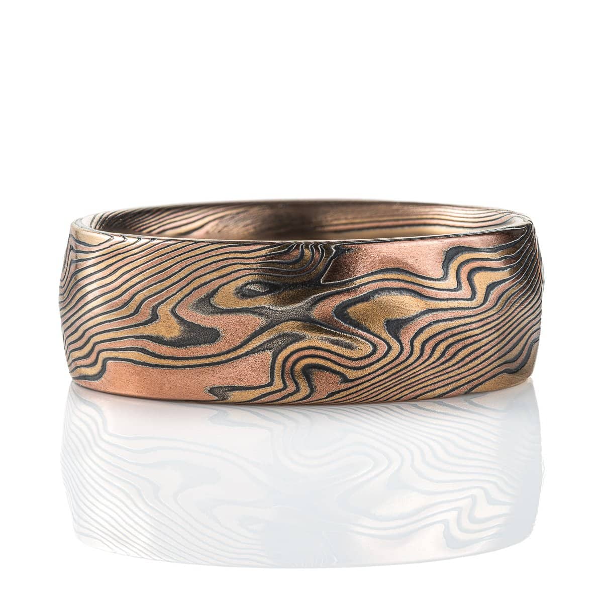 Wide mokume gane patterned ring, made with red and yellow gold and oxidized silver, with added carving to create a rippling, textured effect.