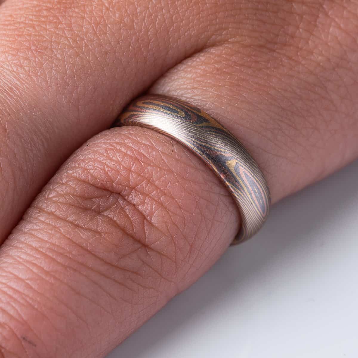 Slim mokume gane patterned ring with angled ellipse shapes running around the band, made with red gold, yellow gold and palladium, domed profile, smooth finish.