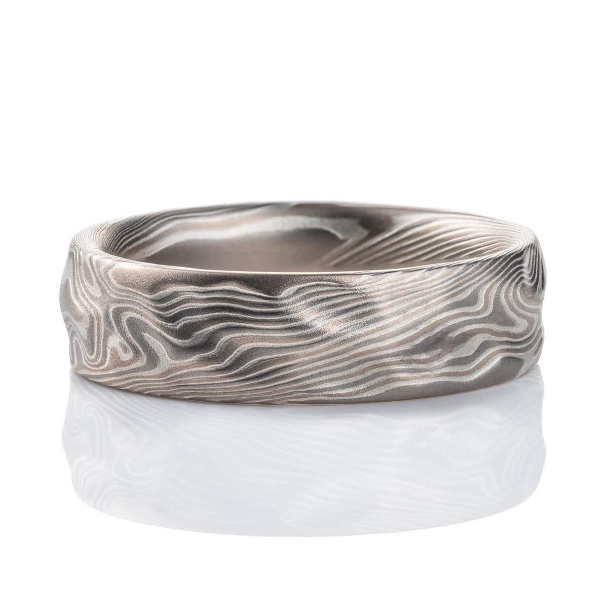 Textured mokume gane patterned ring, with etching and surface carving resembling rough stone, made with layers of light and dark gray metals.