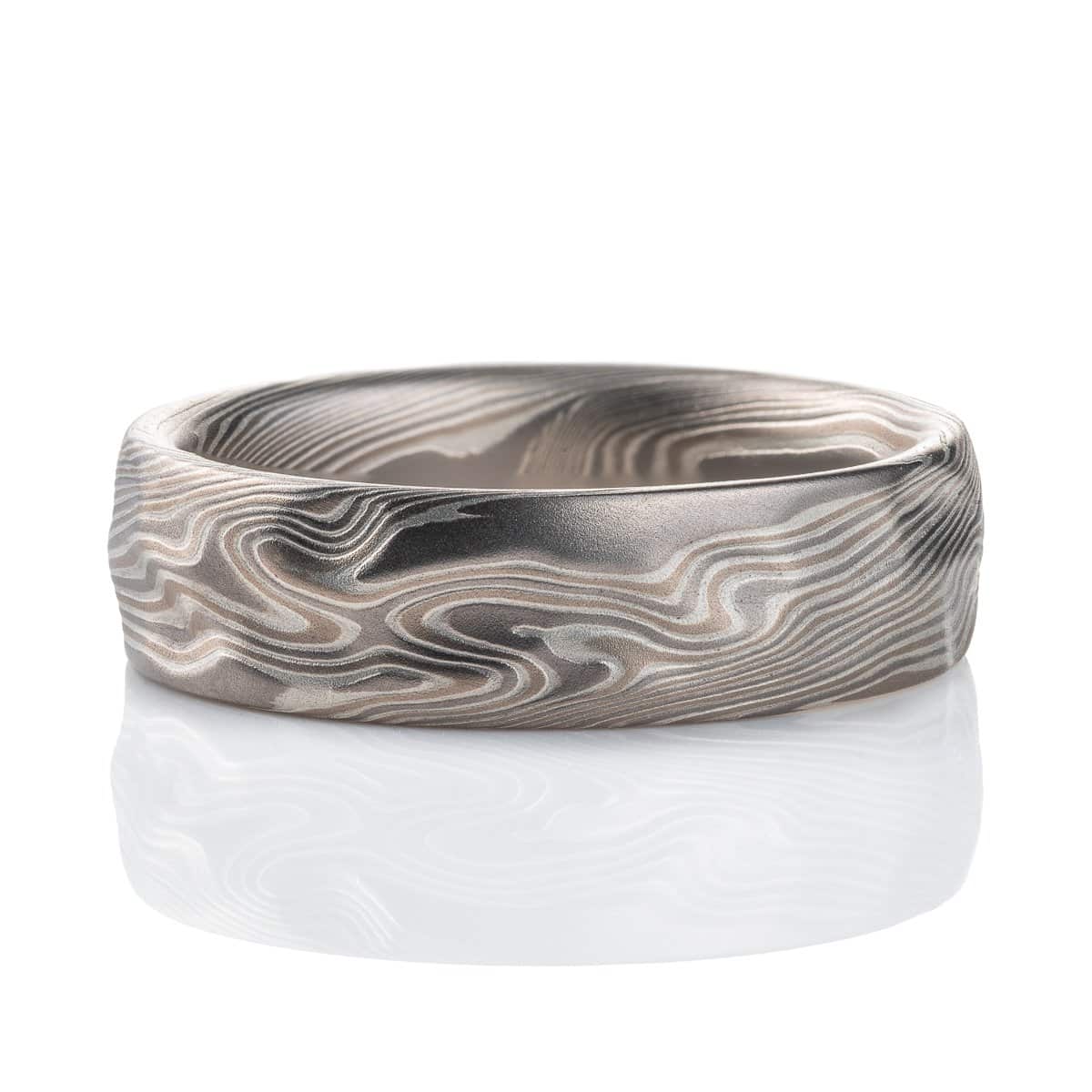 Textured mokume gane patterned ring, with etching and surface carving resembling rough stone, made with layers of light and dark gray metals.
