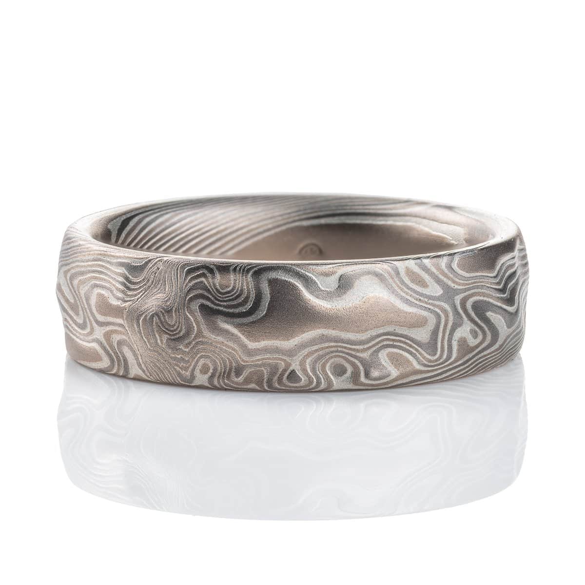 Textured mokume gane patterned ring, with etching and surface carving resembling rough stone, made with layers of light and dark gray metals.