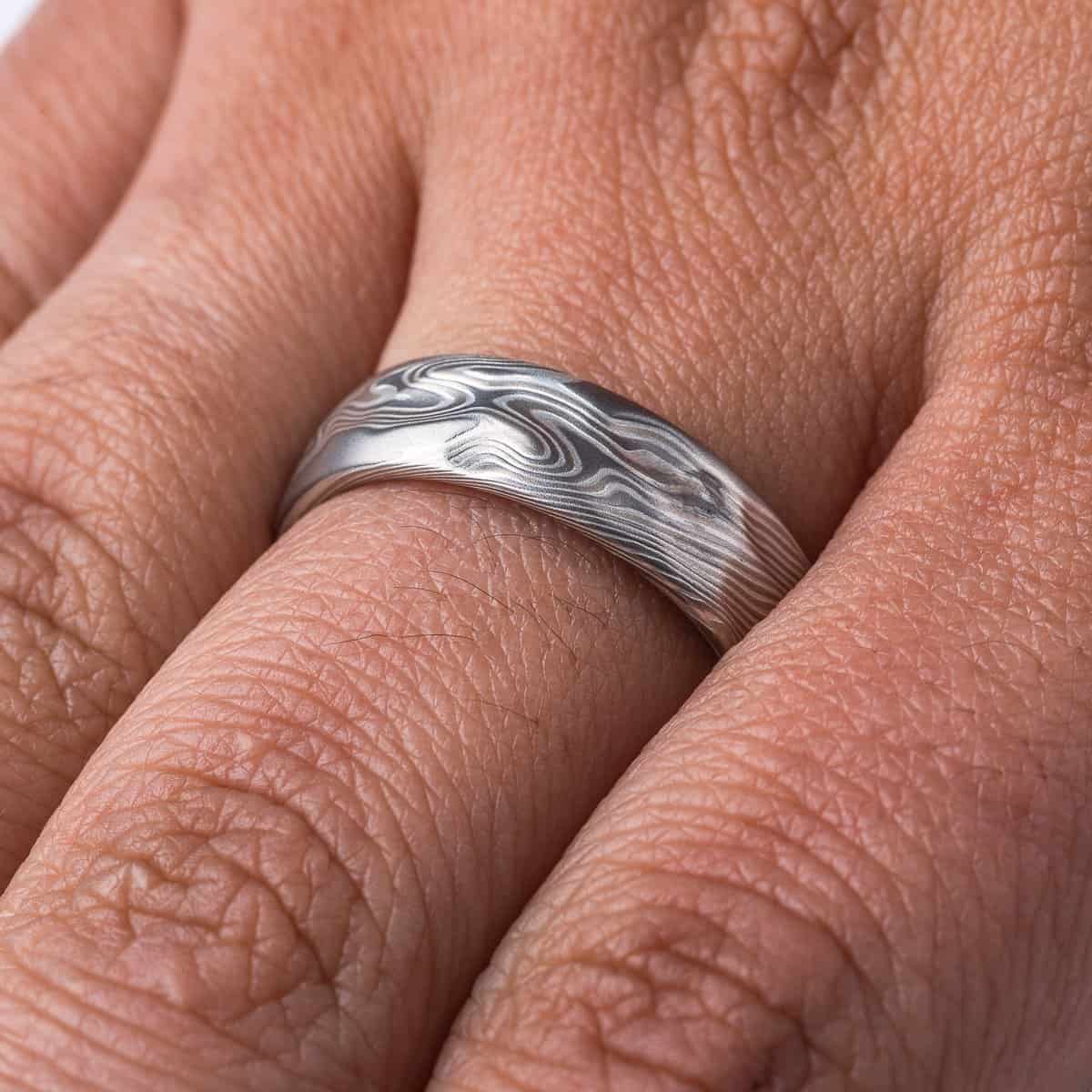Textured mokume gane patterned ring, with etching and surface carving resembling rough stone, made with layers of light and dark gray metals.