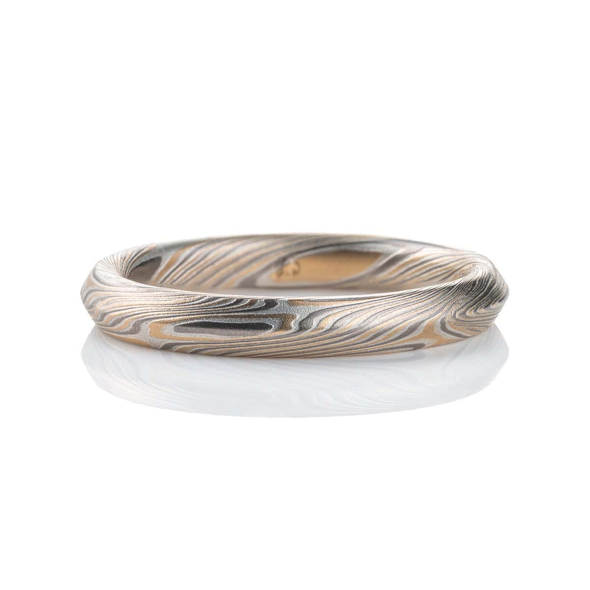 Mokume gane ring with beveled profile, patterned in long swooping lines and starburst like arcs. Made with yellow gold, silver and palladium.