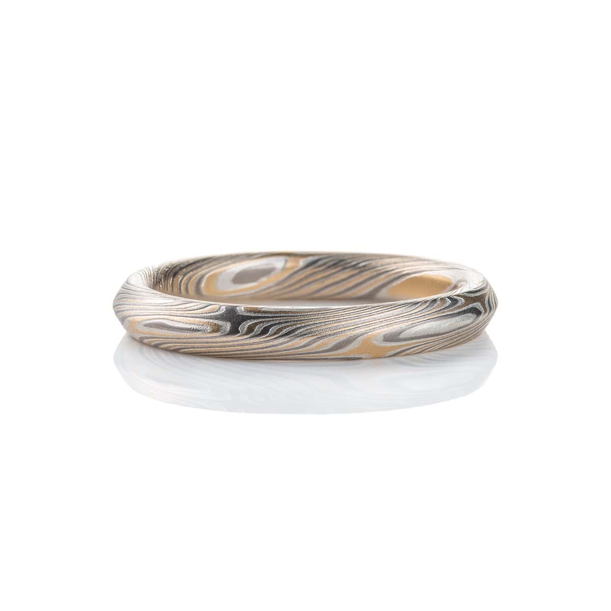 Mokume gane ring with beveled profile, patterned in long swooping lines and starburst like arcs. Made with yellow gold, silver and palladium.